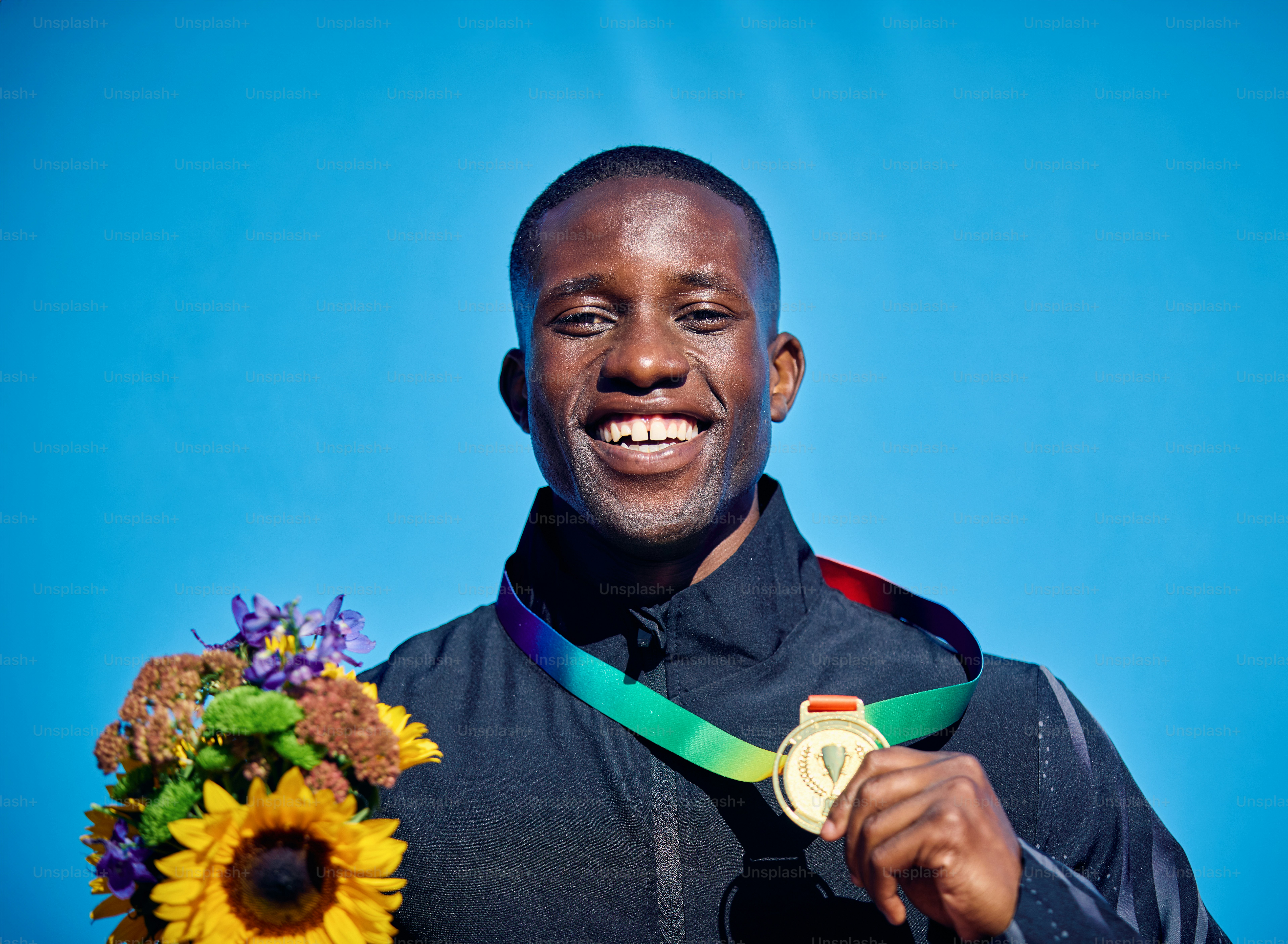 Proud athlete displaying medal with sunflower bouquet. Outdoor celebration portrait with blue sky background. Sports victory and happiness concept.