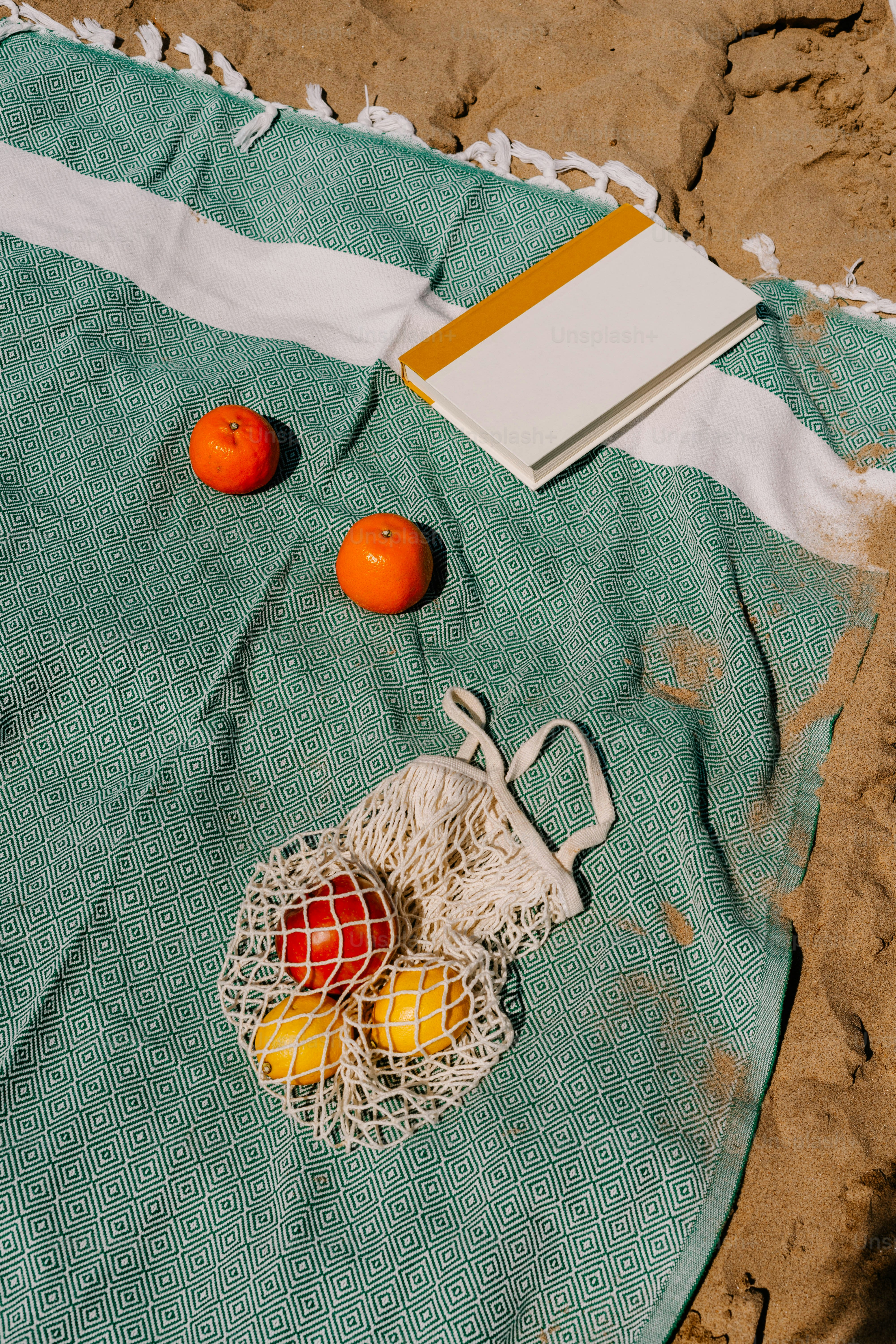 Two oranges and a book on a towel on the beach