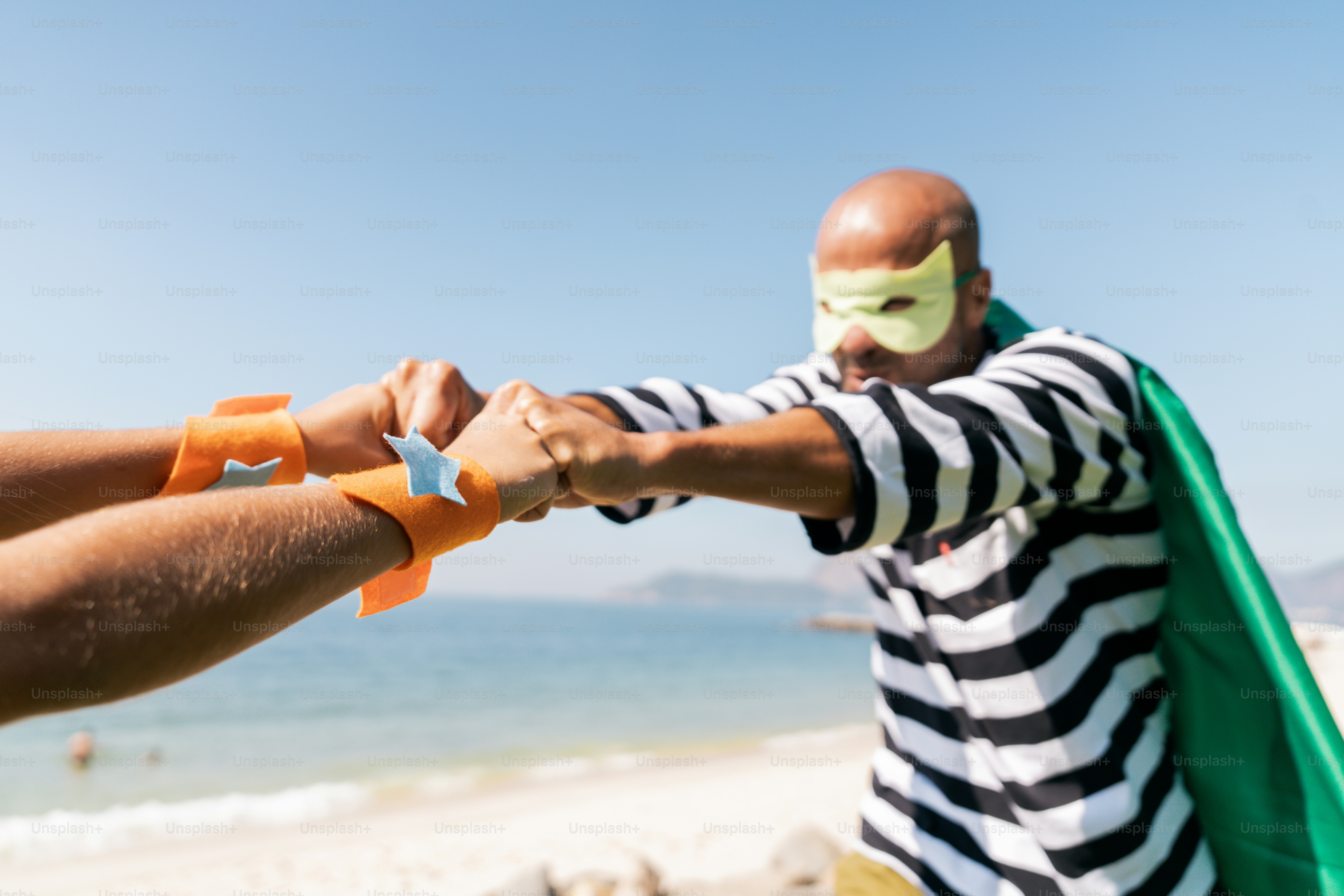 A man in a striped shirt is holding a man in a green cape