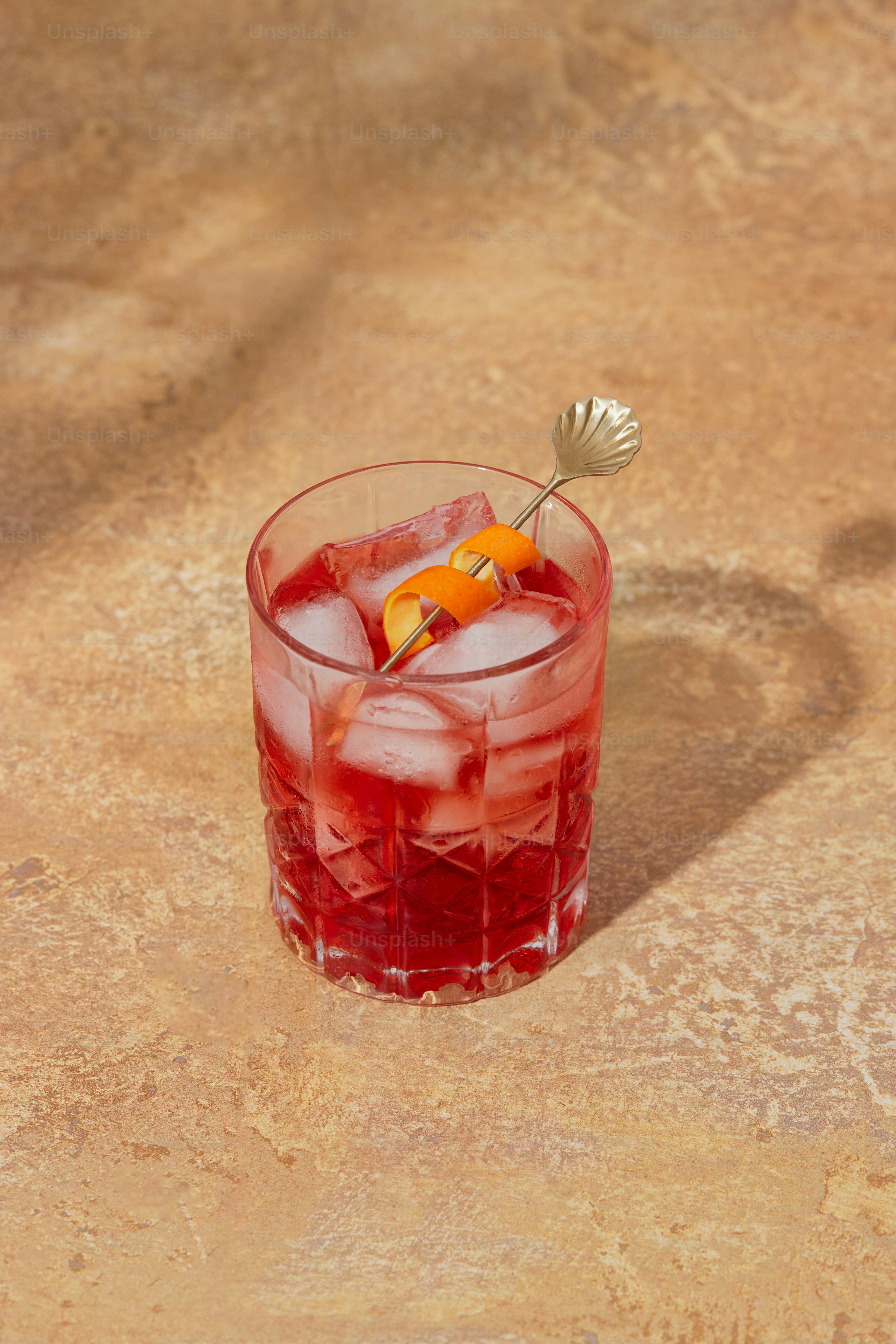A red drink with a orange garnish in a glass