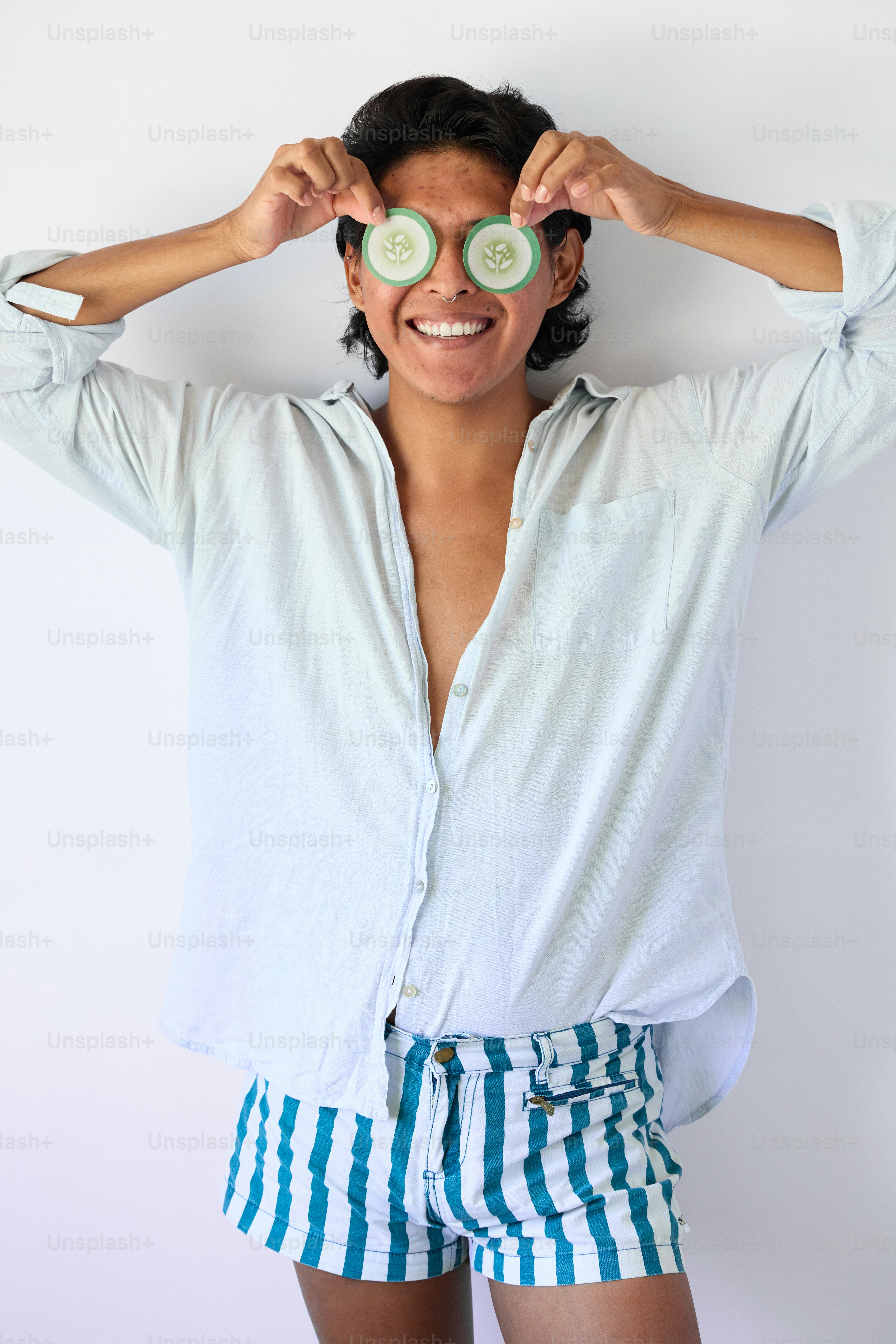 A woman holding two cucumbers over her eyes