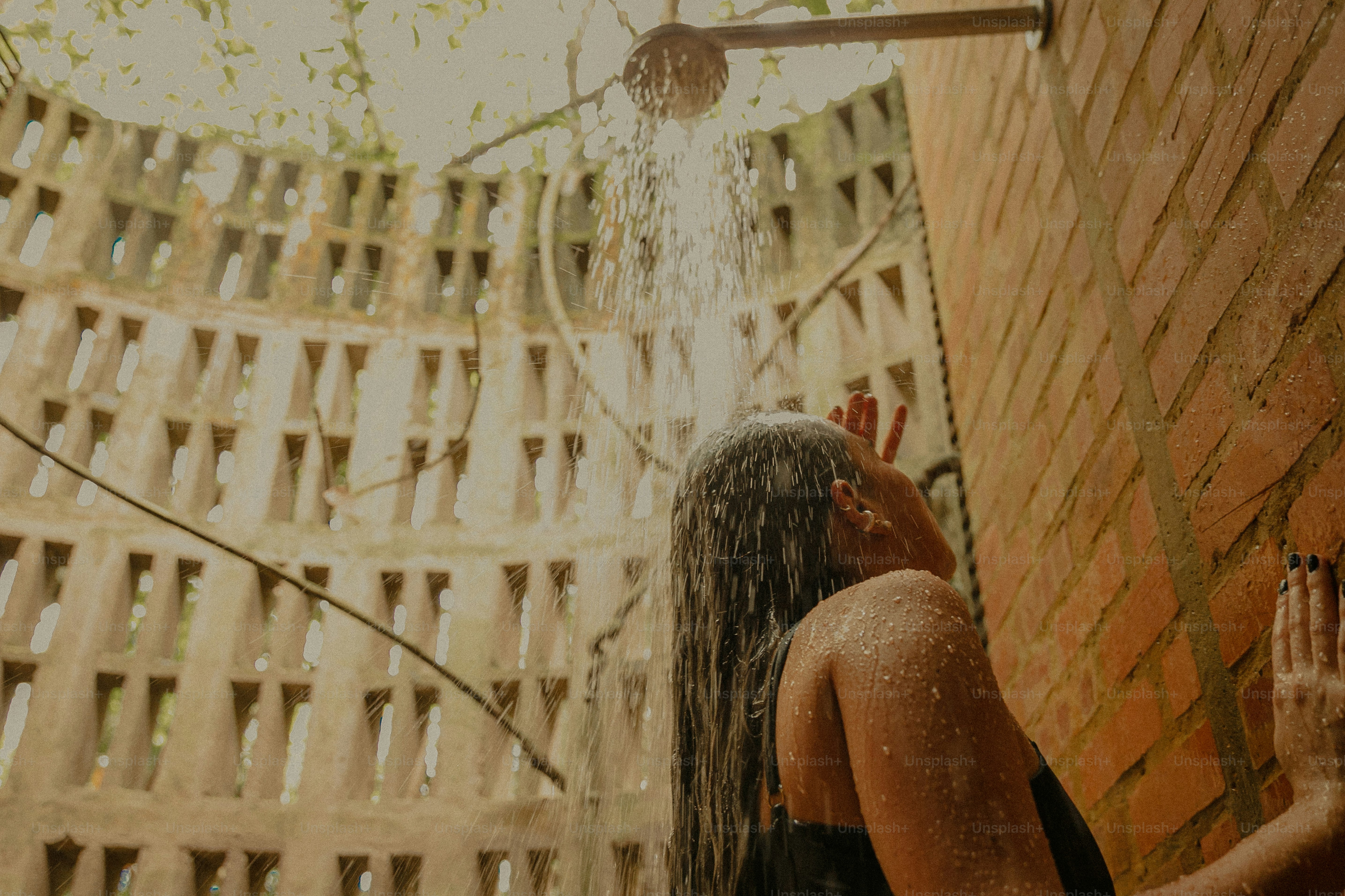 A woman in a black bathing suit is spraying water from a shower head