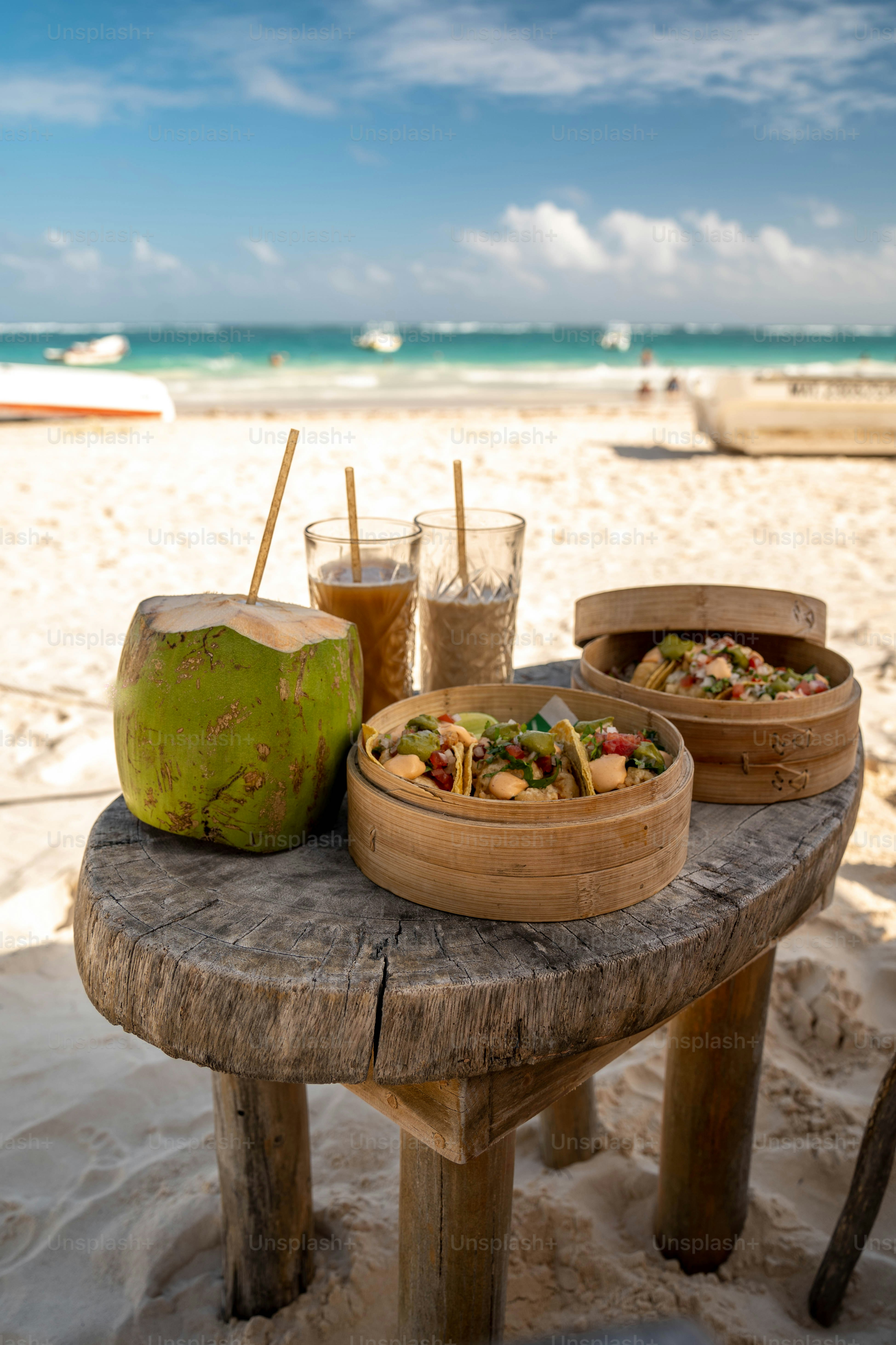 Uma mesa de madeira coberta com tigelas de comida em cima de uma praia arenosa