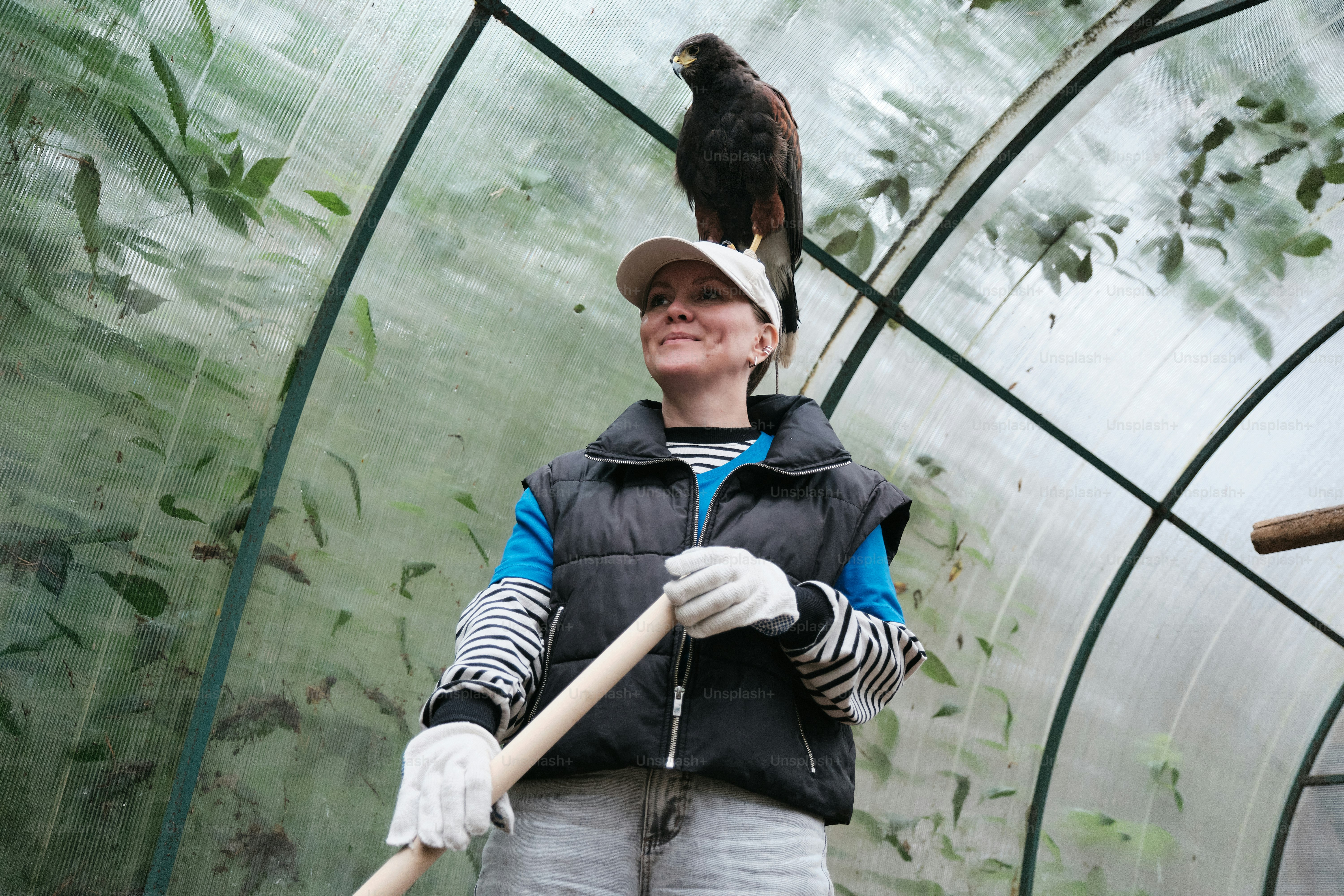 A woman holding a stick and a bird on her shoulder