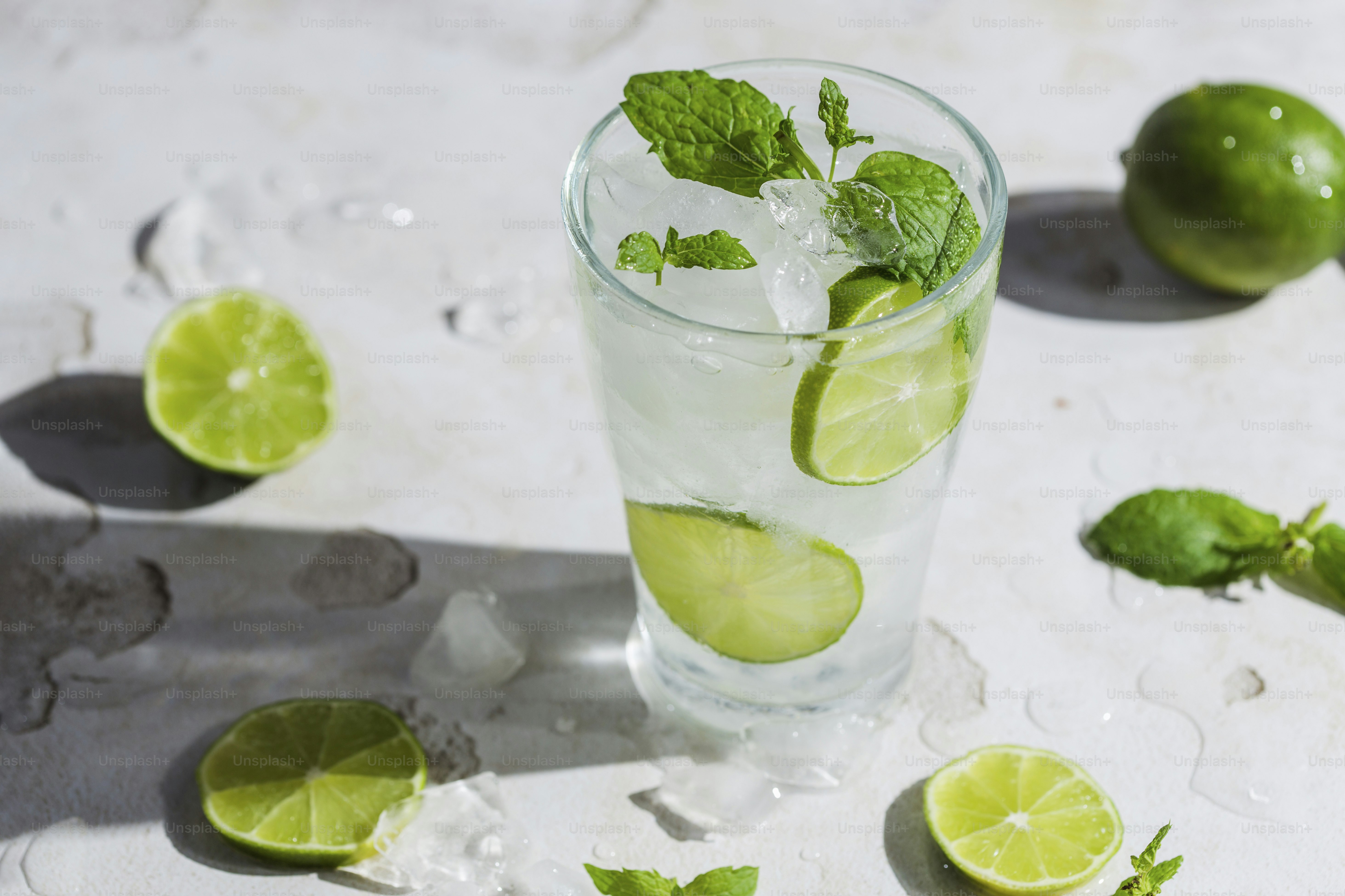 A glass of water with limes and mints around it