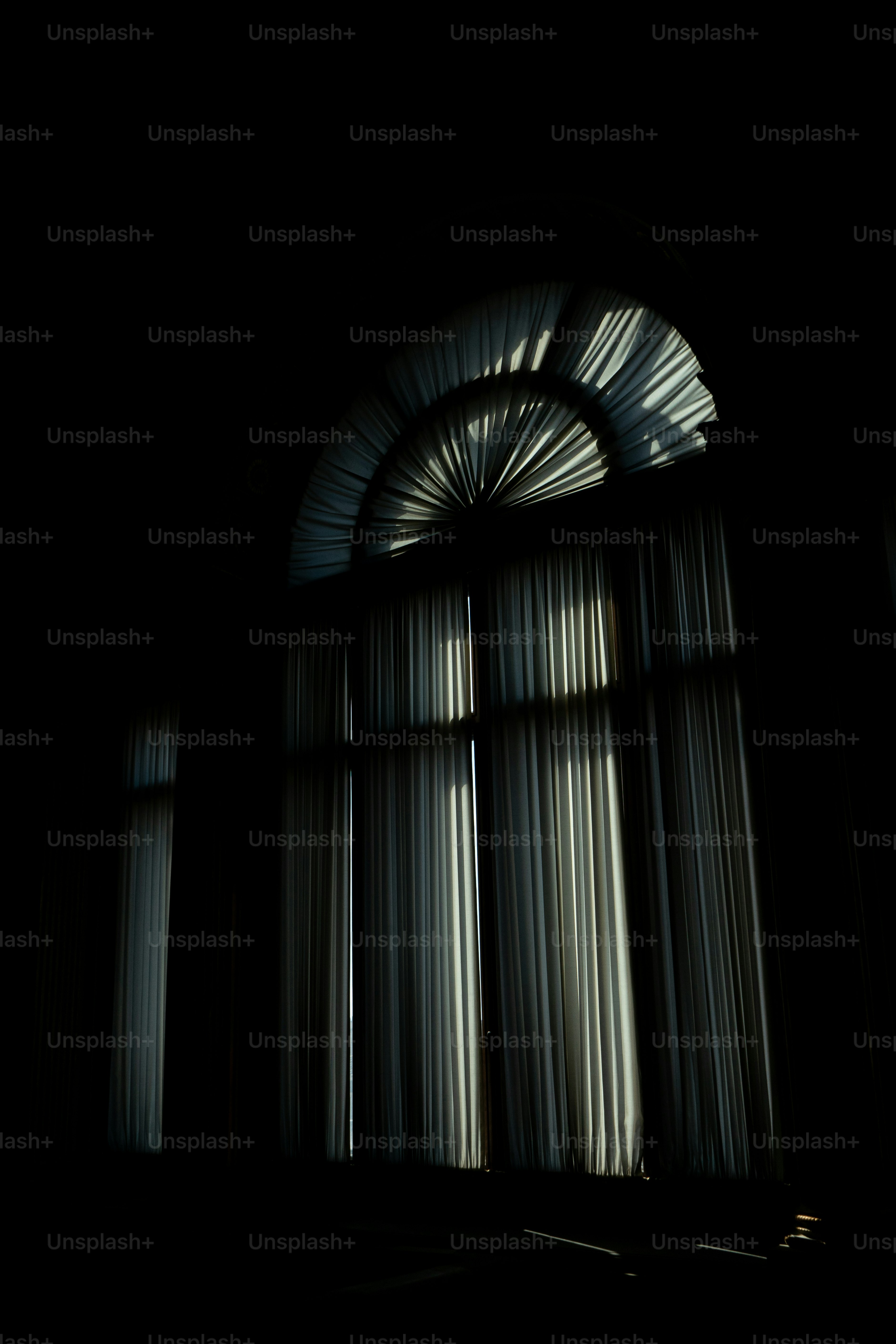A dark room with a large window and curtains