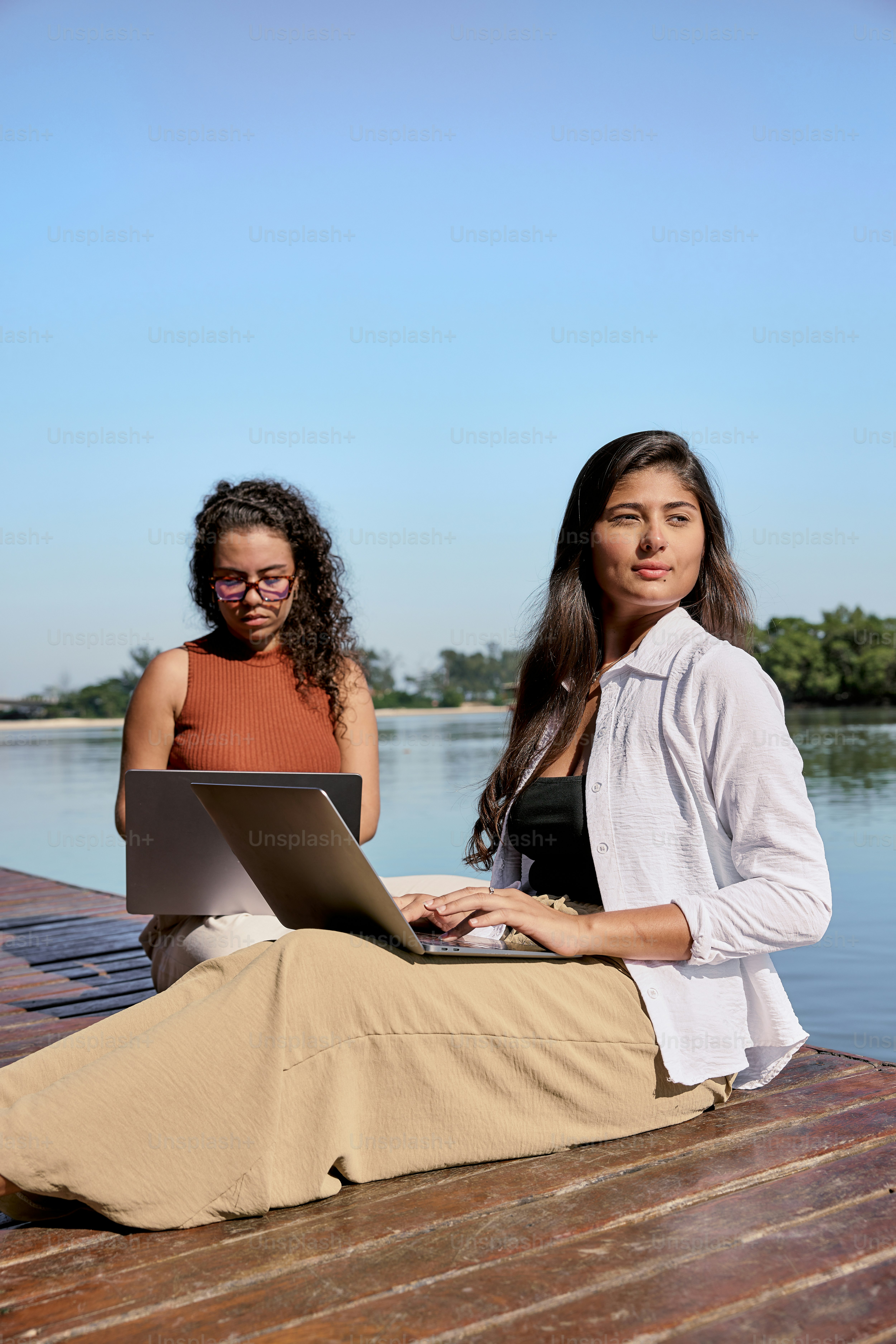 Two women sitting on a dock with a laptop