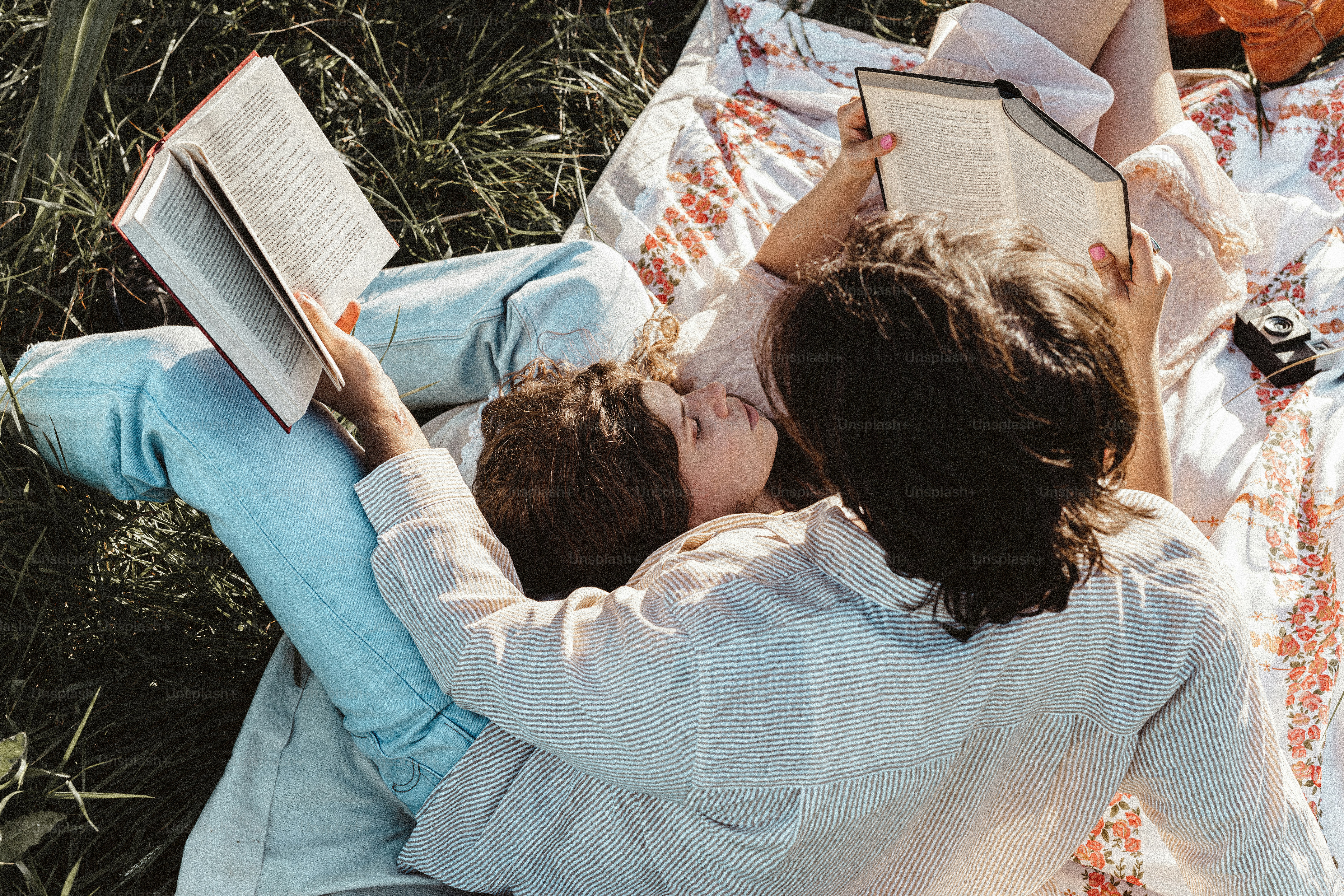 Two people laying on a blanket reading a book