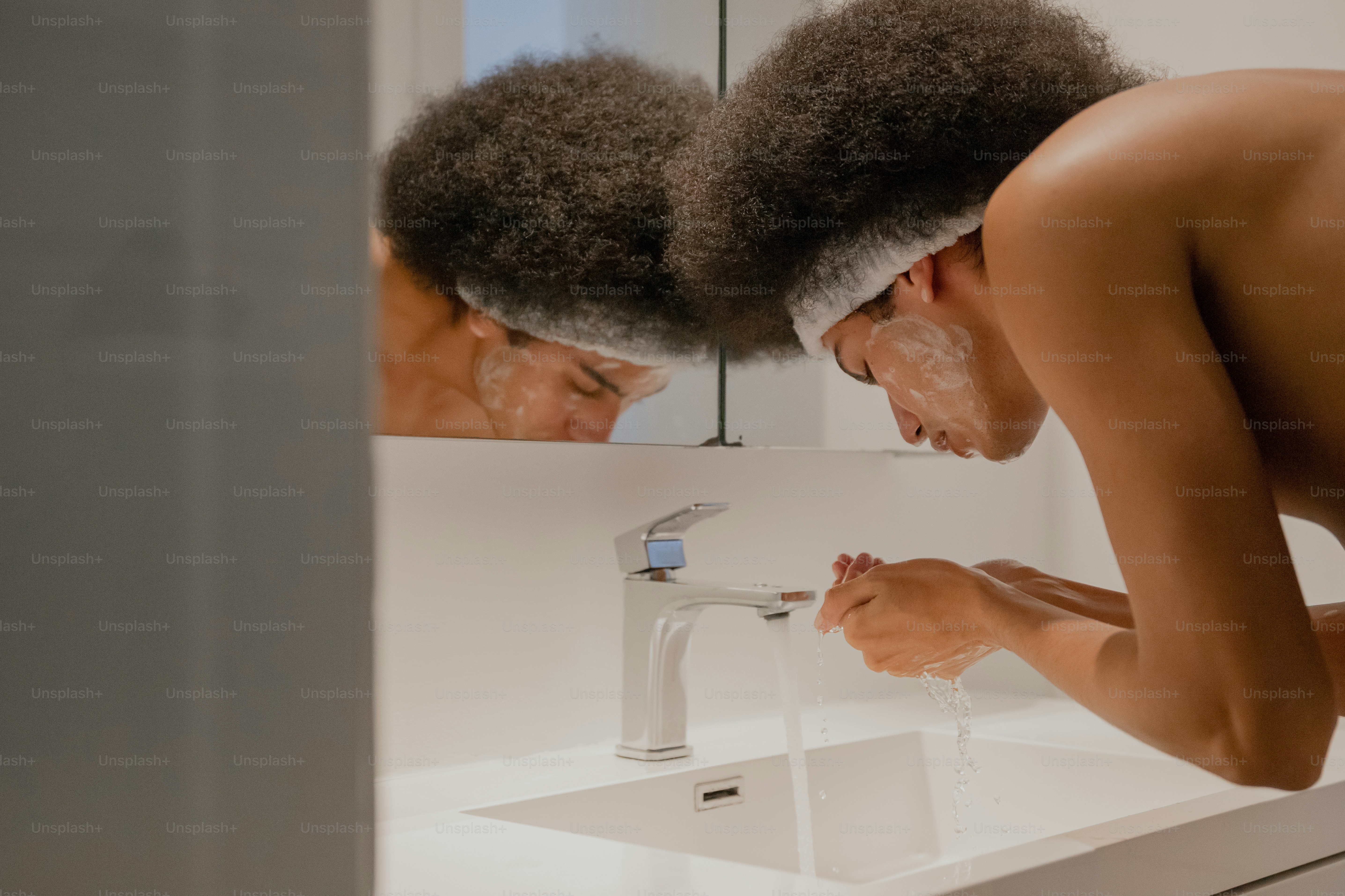 A shirtless man standing in front of a bathroom mirror