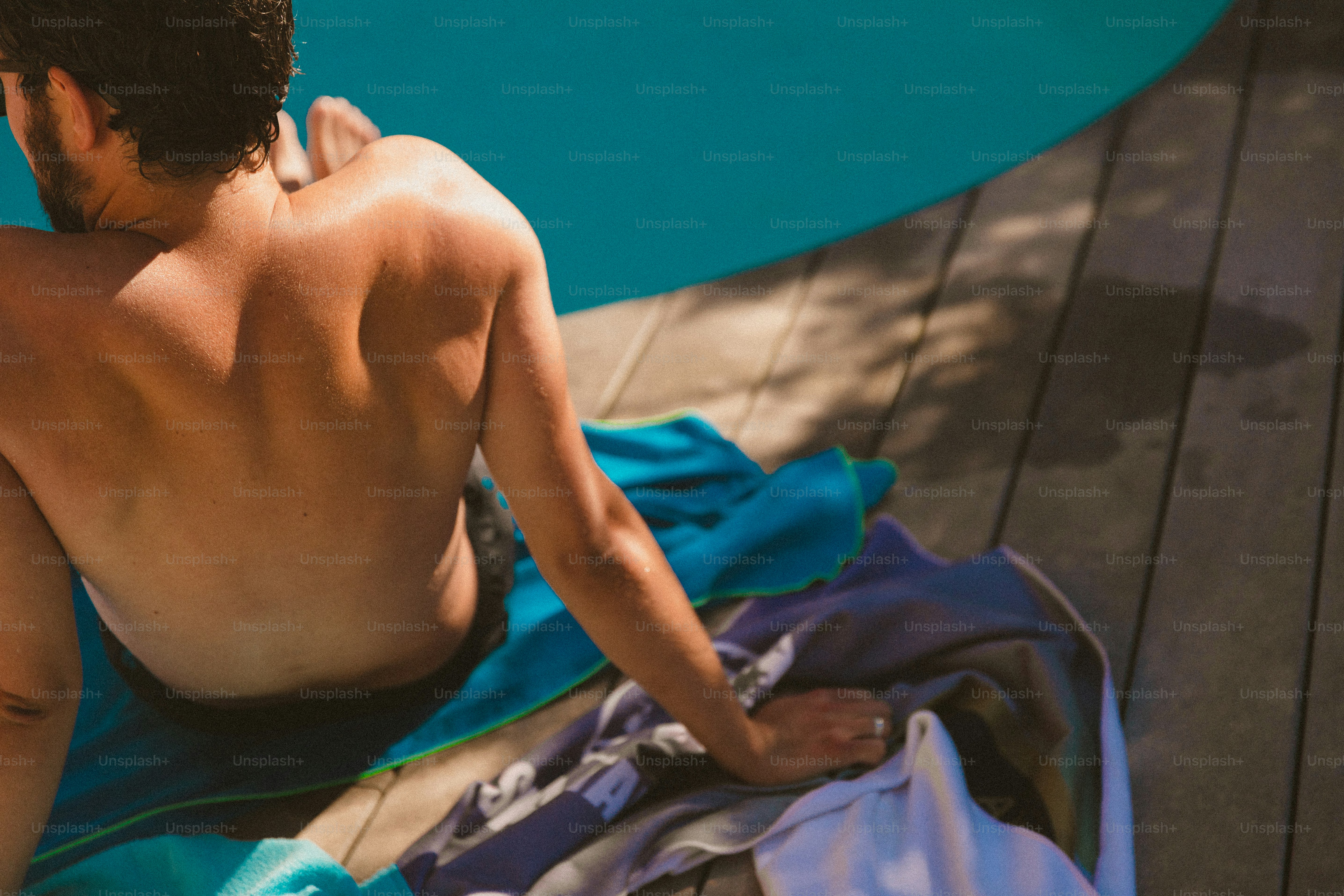 A man sitting on a towel next to a swimming pool