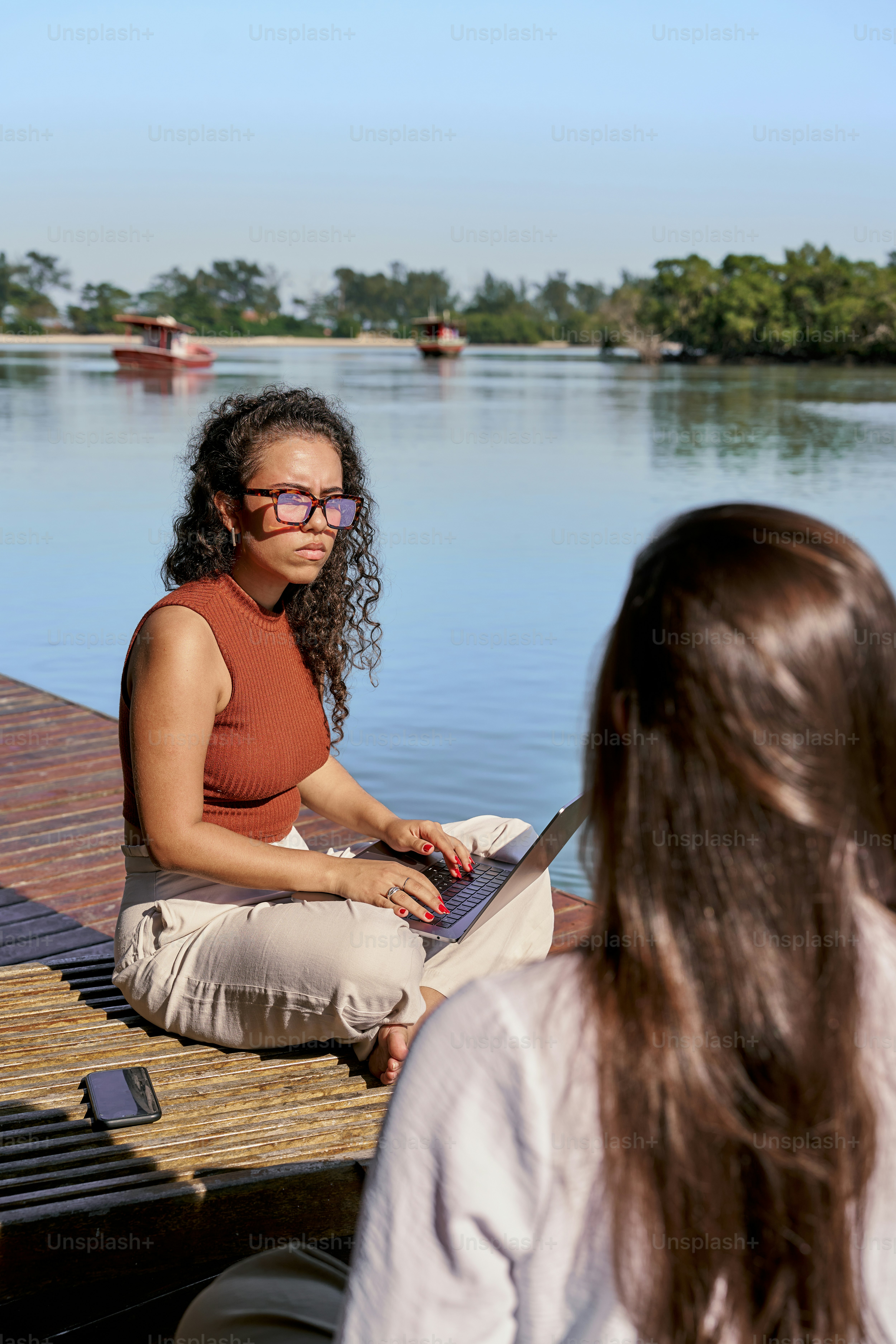 A woman sitting on a dock using a laptop computer