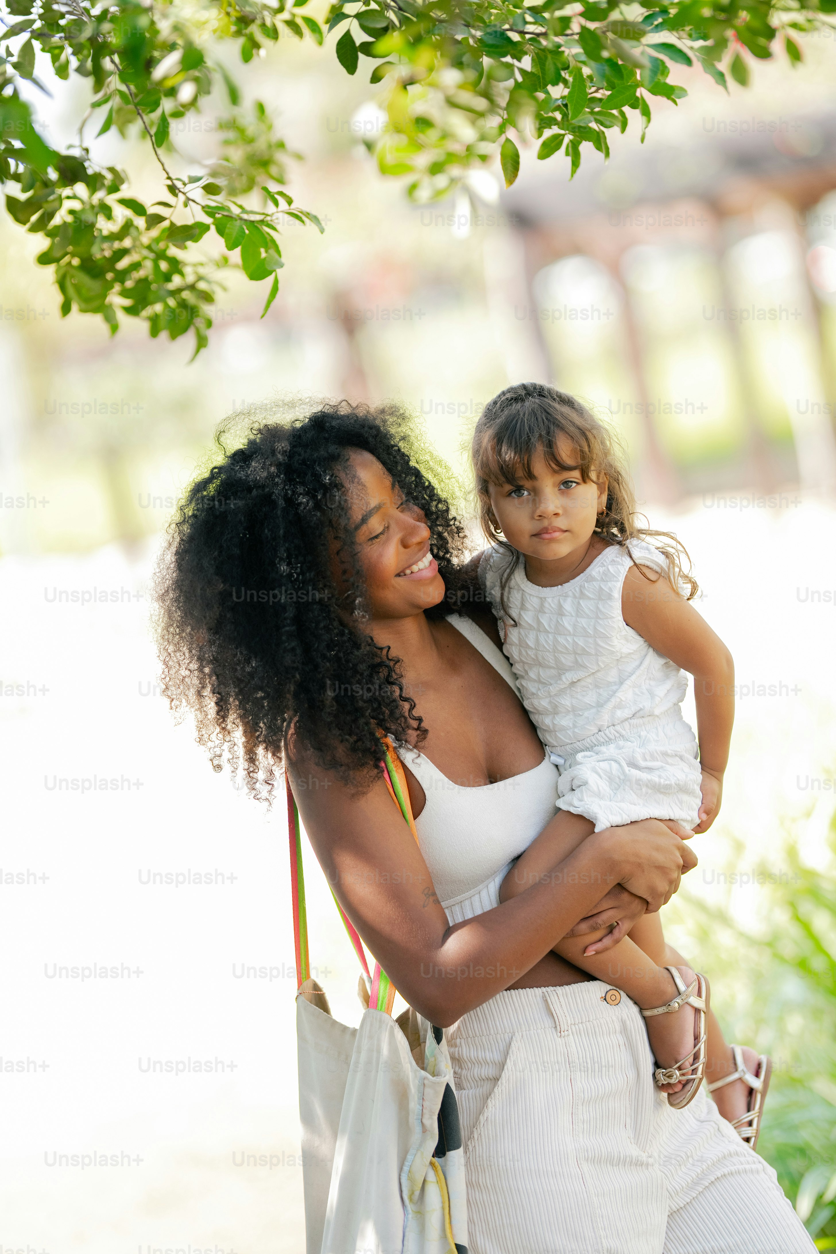 A woman holding a little girl under a tree