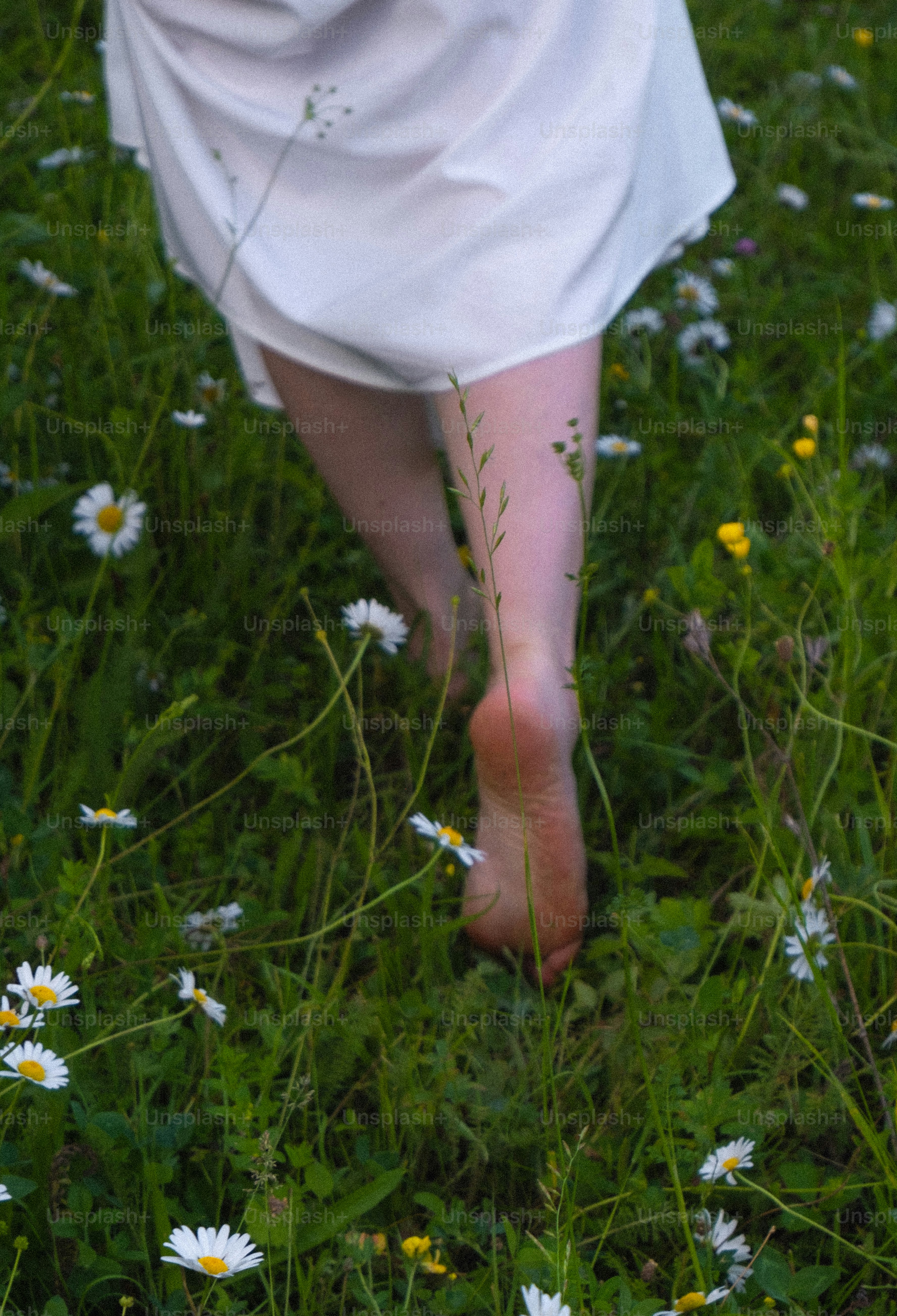A woman in a white dress walking through a field of daisies
