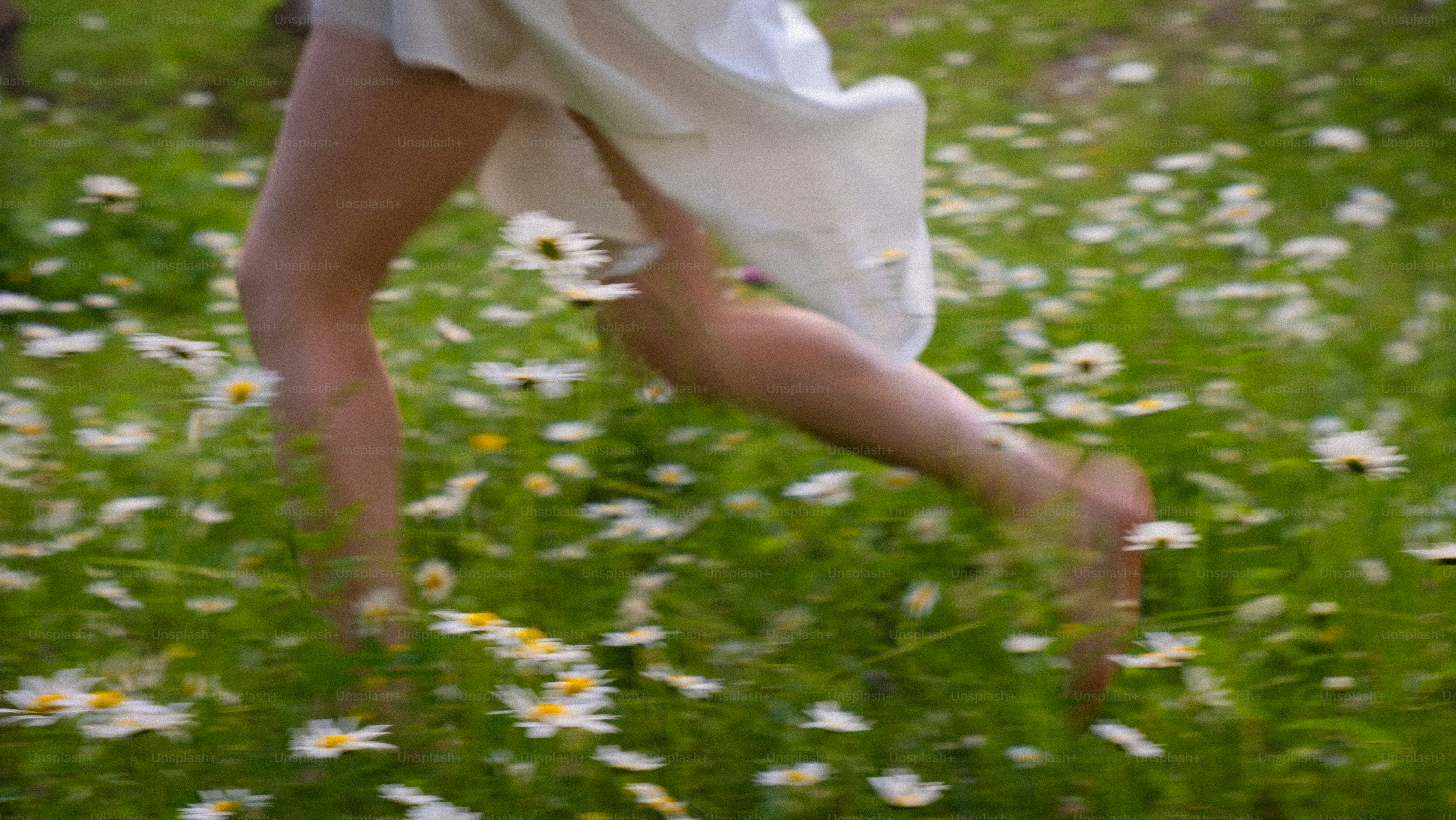 A woman in a white dress running through a field of daisies