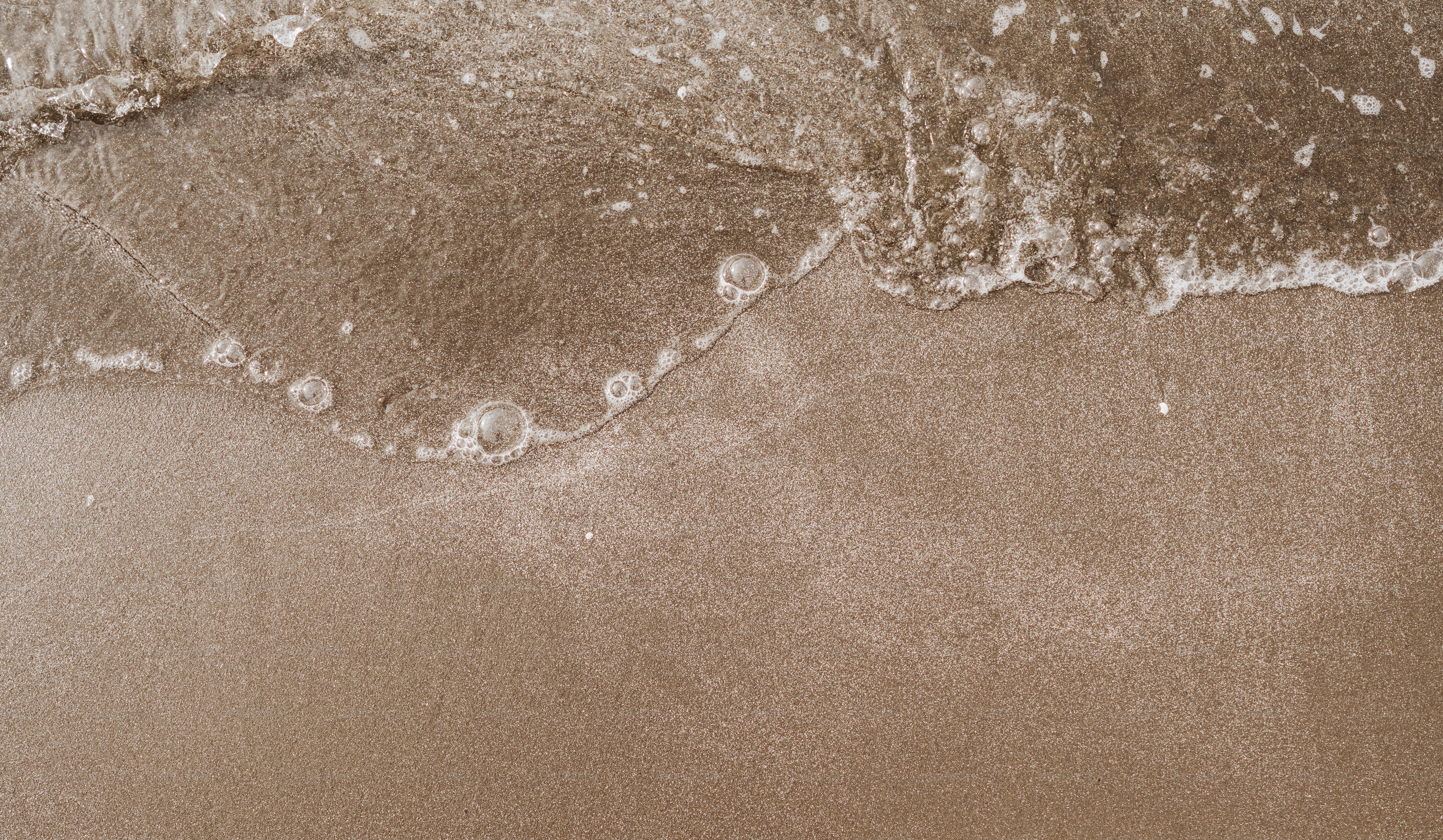 A sandy beach with waves coming in and out of the water