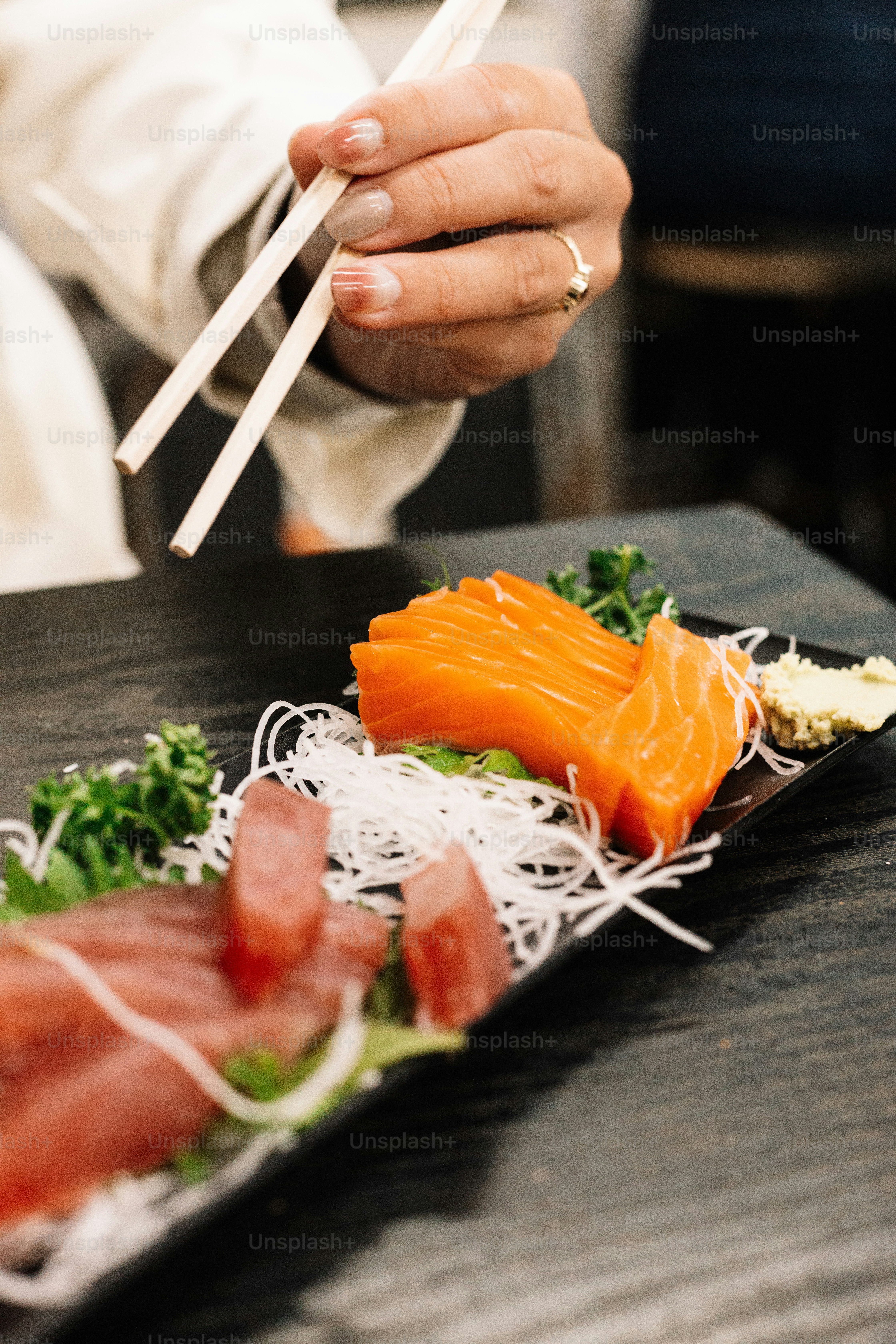 Una persona sosteniendo palillos sobre un plato de sushi