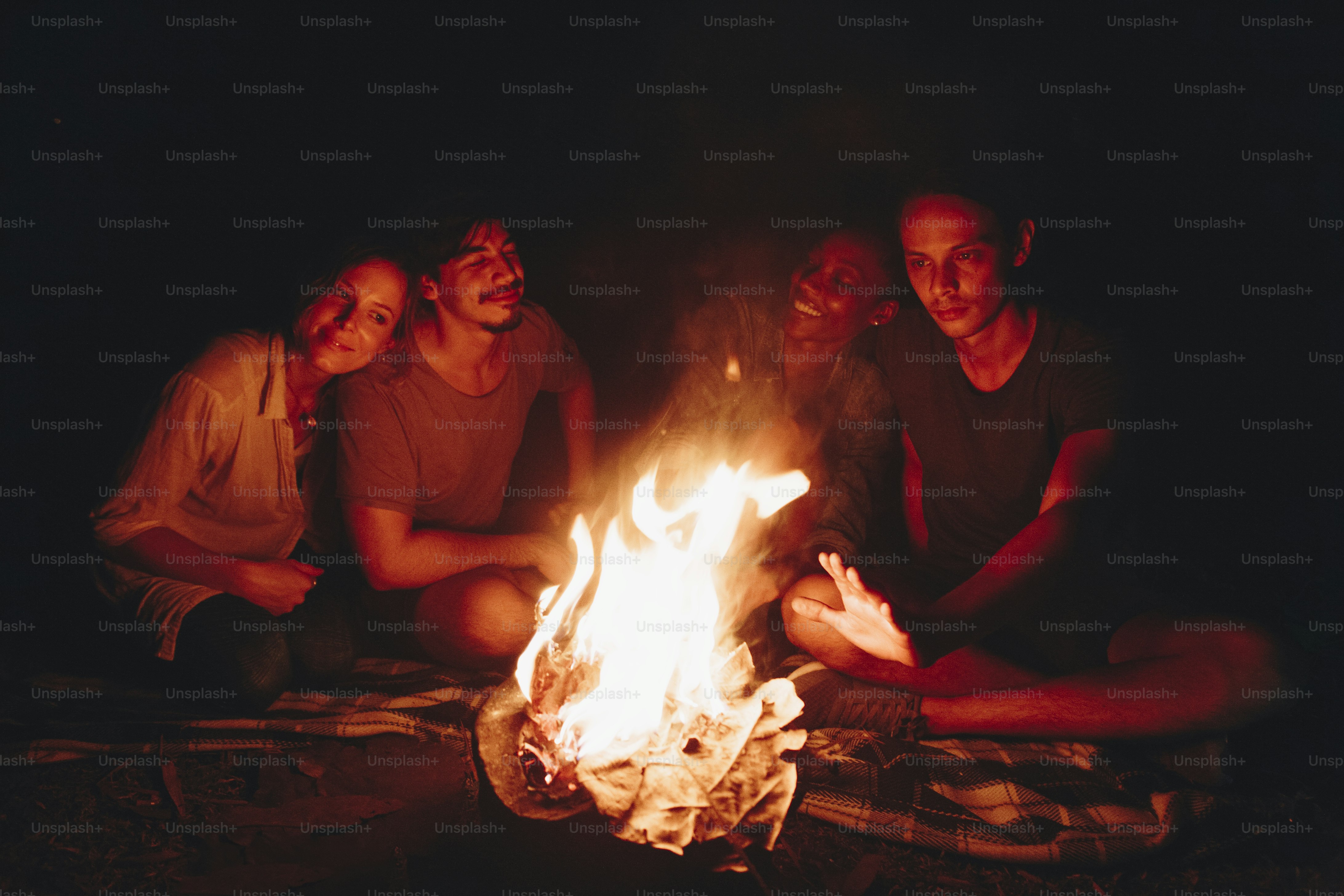 Group of young adult friends sitting around the bonfire outdoors recreational leisure and friendship concept