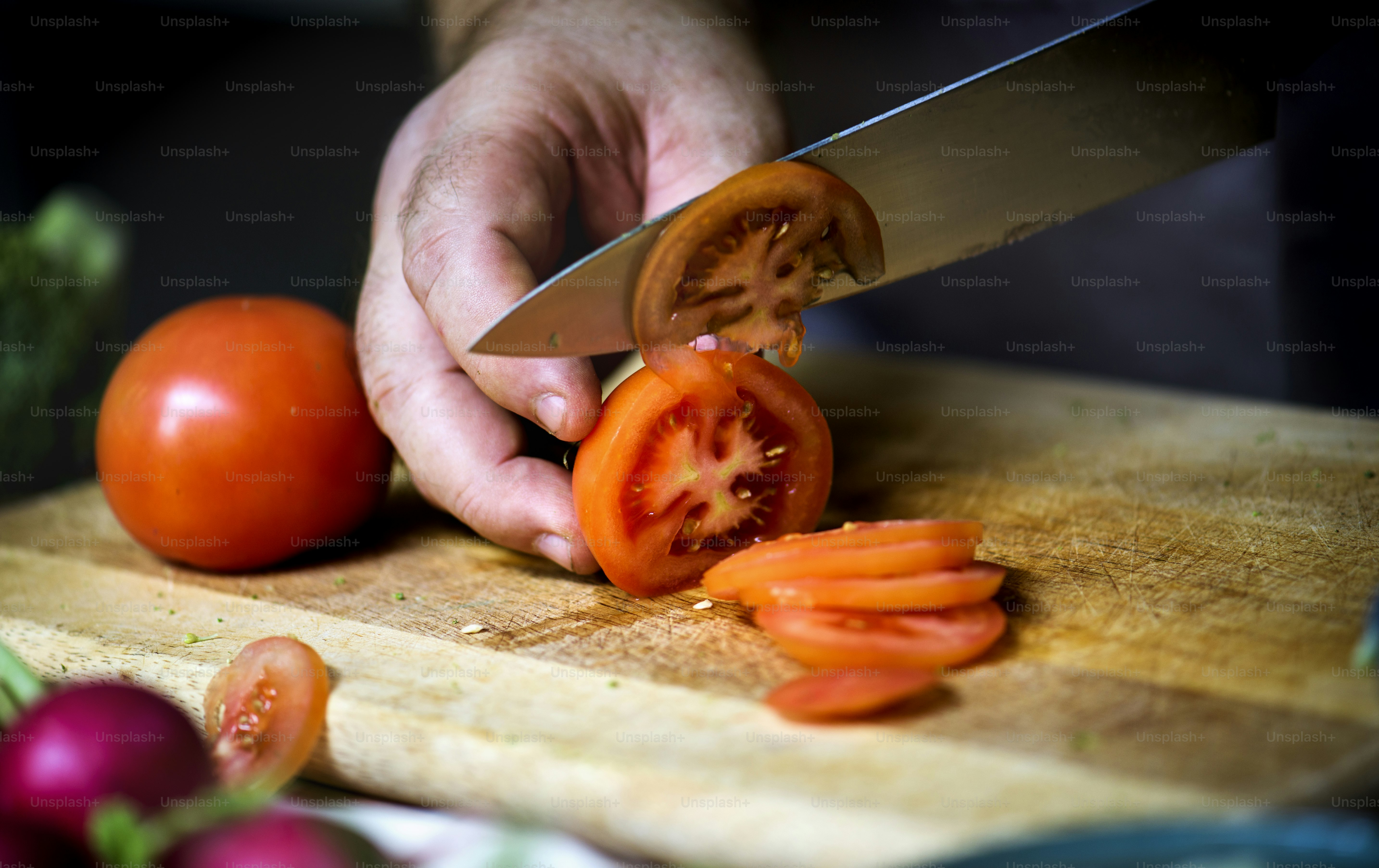 Primer plano de la mano con el cuchillo cortando tomate vegetal fresco