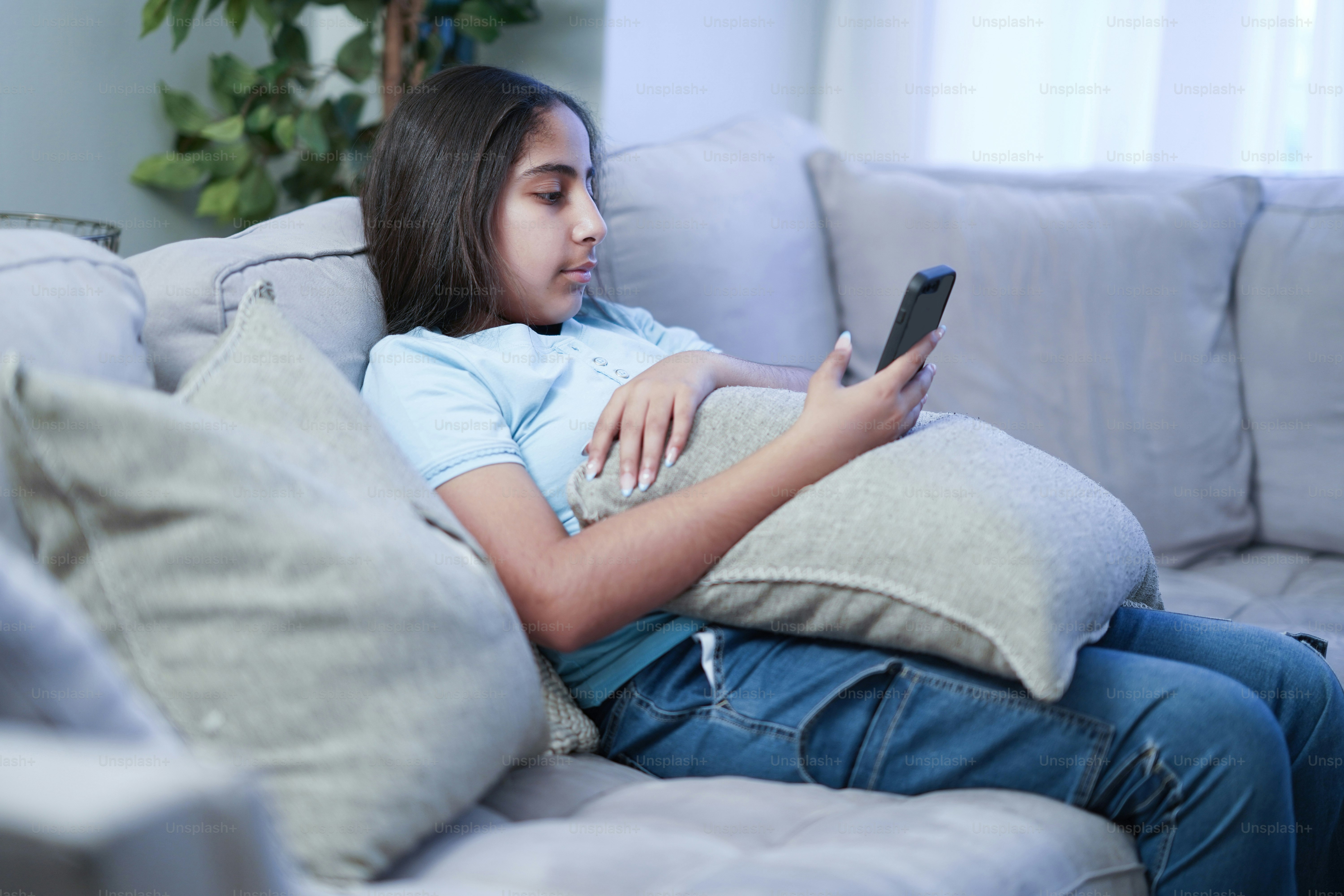 A girl sitting on a couch looking at her cell phone photo – Tweens ...