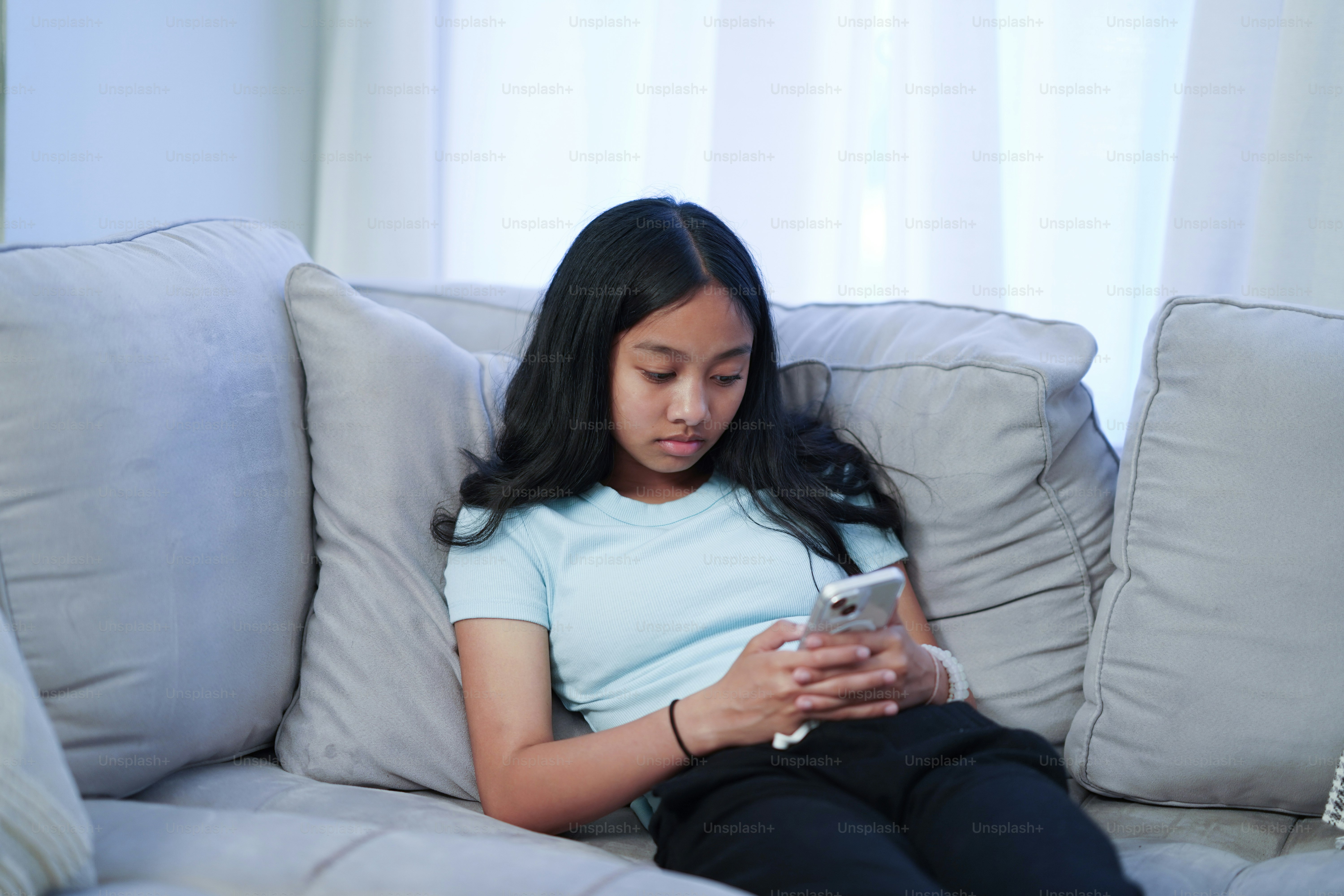A girl sitting on a couch looking at her cell phone photo – Tweens ...