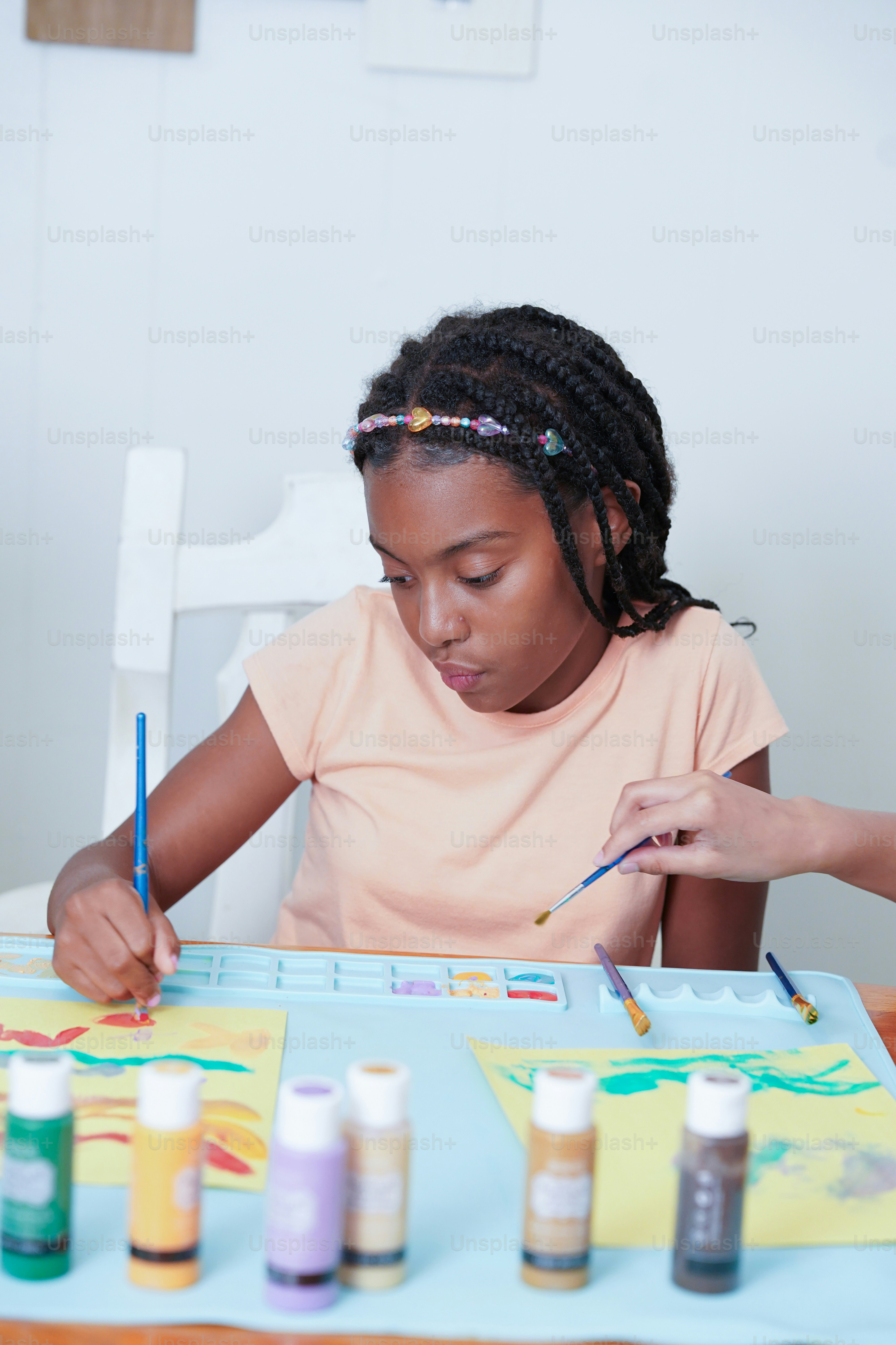 A young girl sitting at a table with paints on it