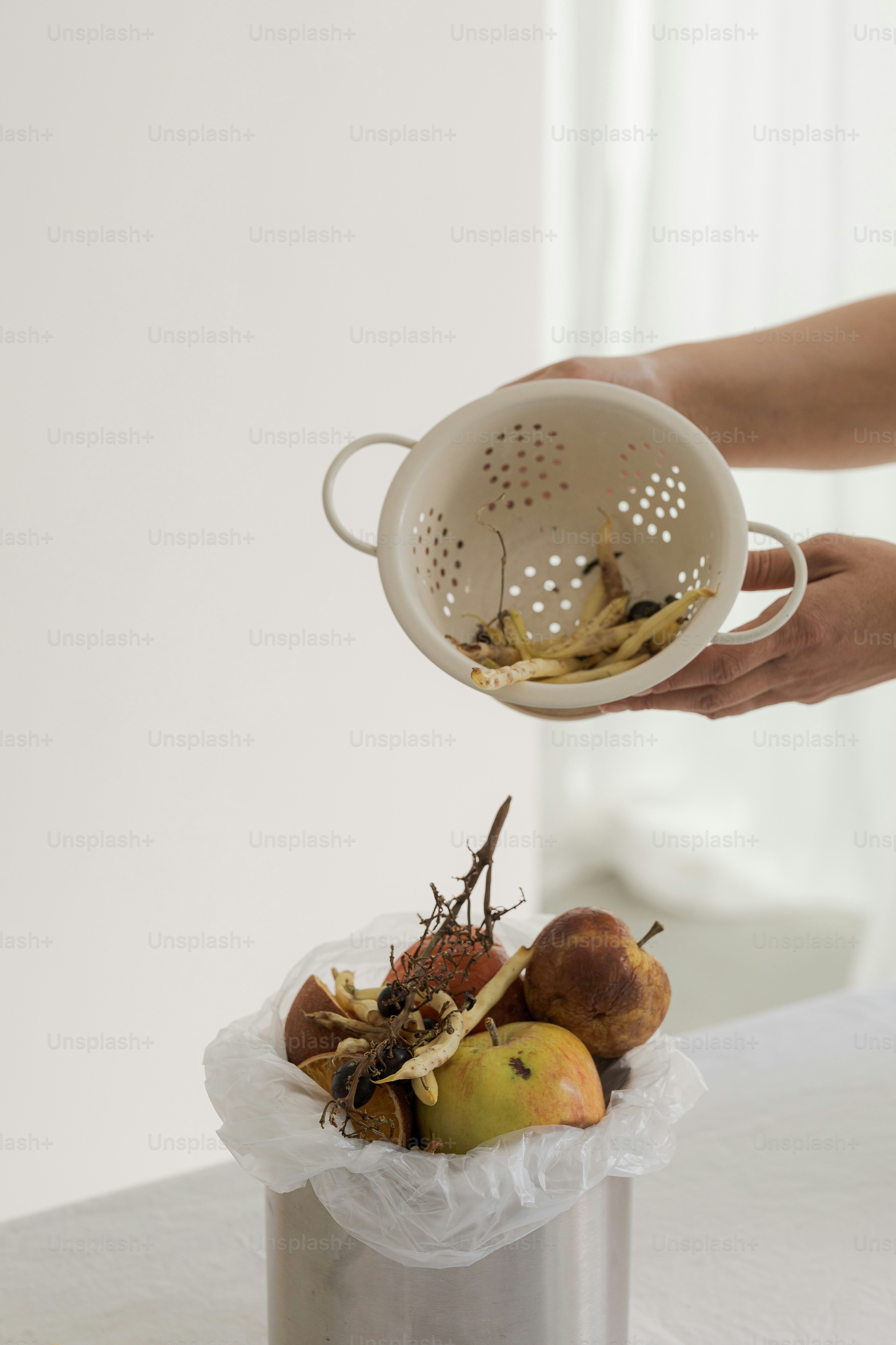 A woman is holding a strainer over a trash can