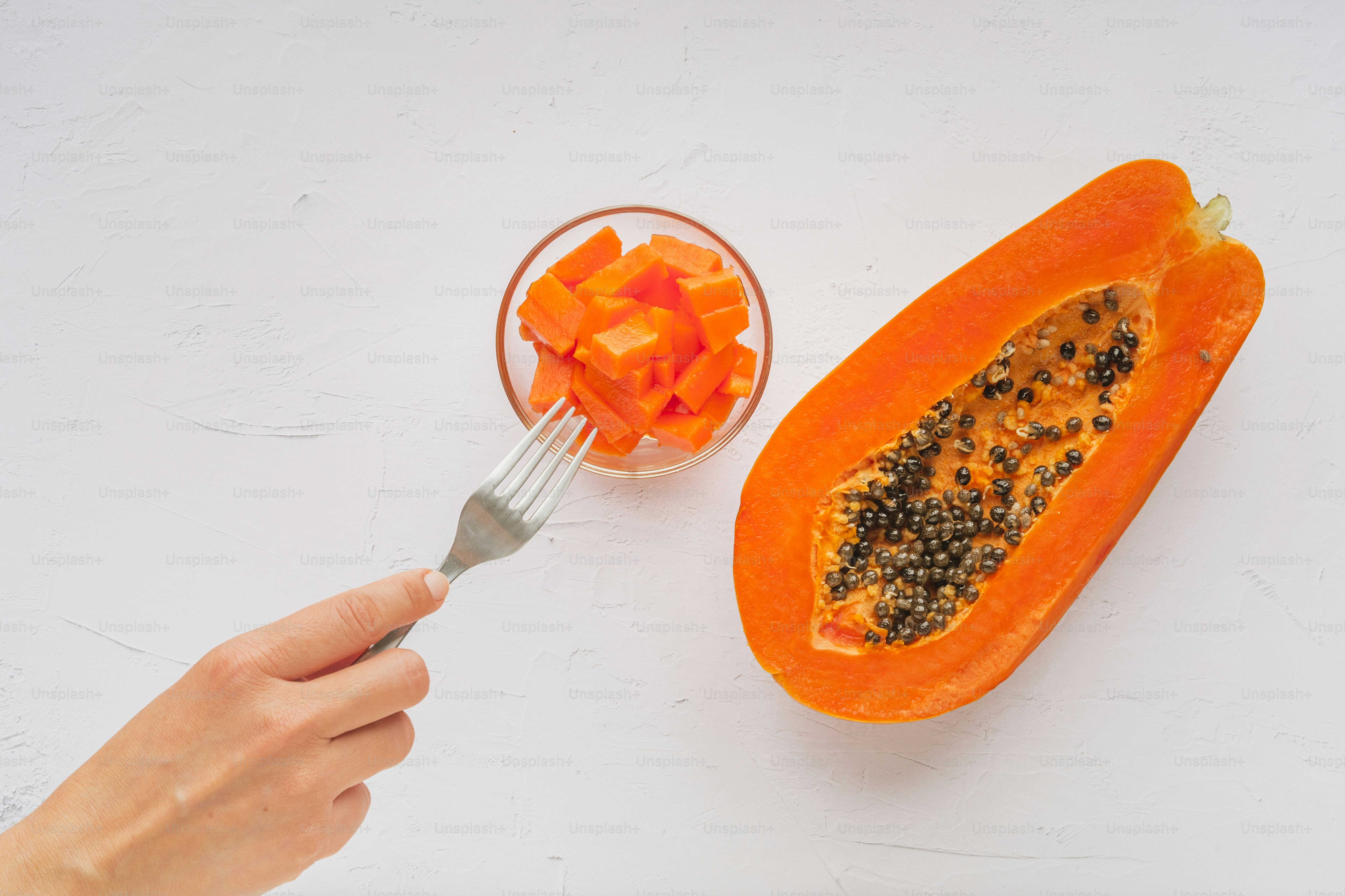 A person holding a spoon over a cut up papaya