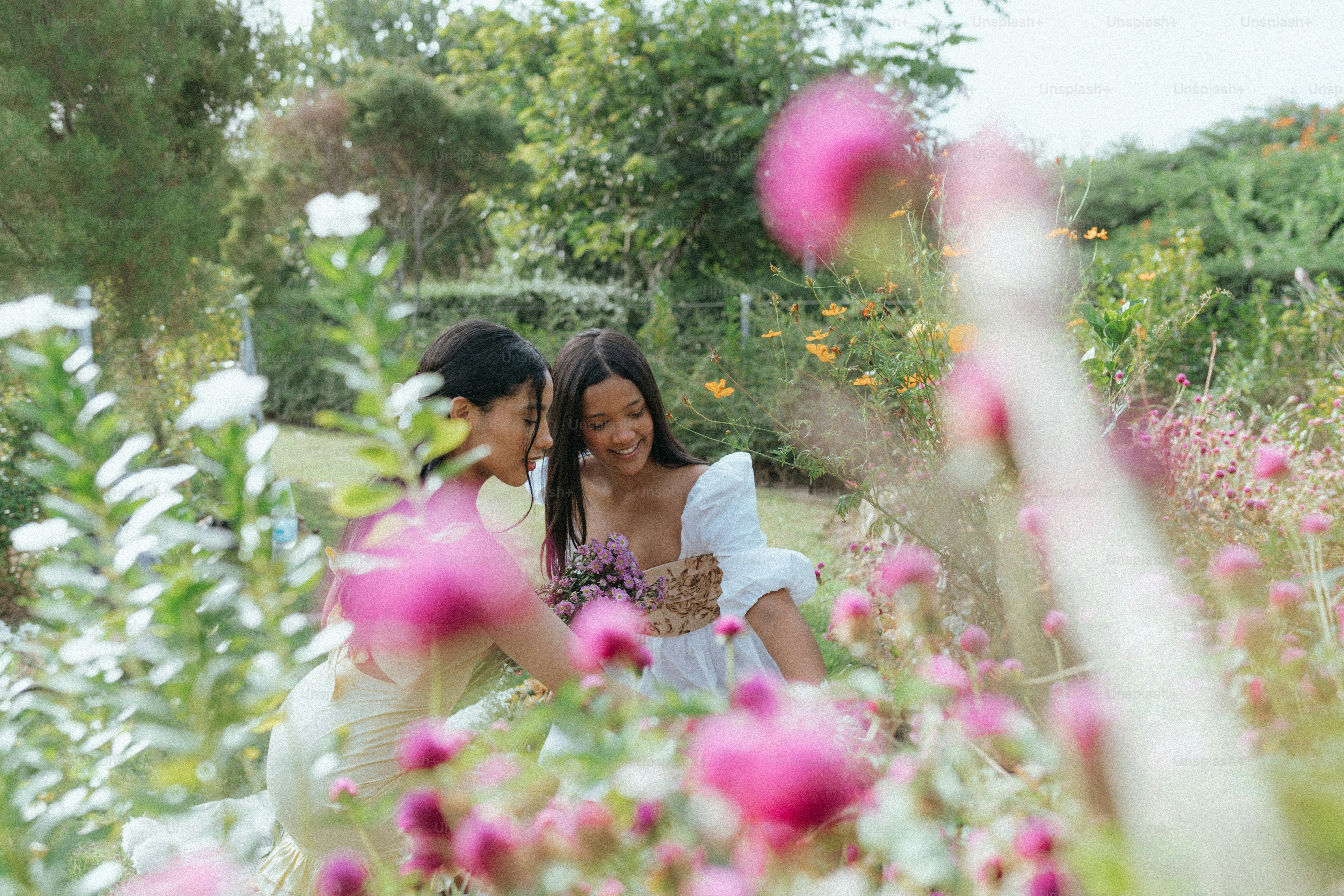 A couple of women standing next to each other in a field of flowers ...