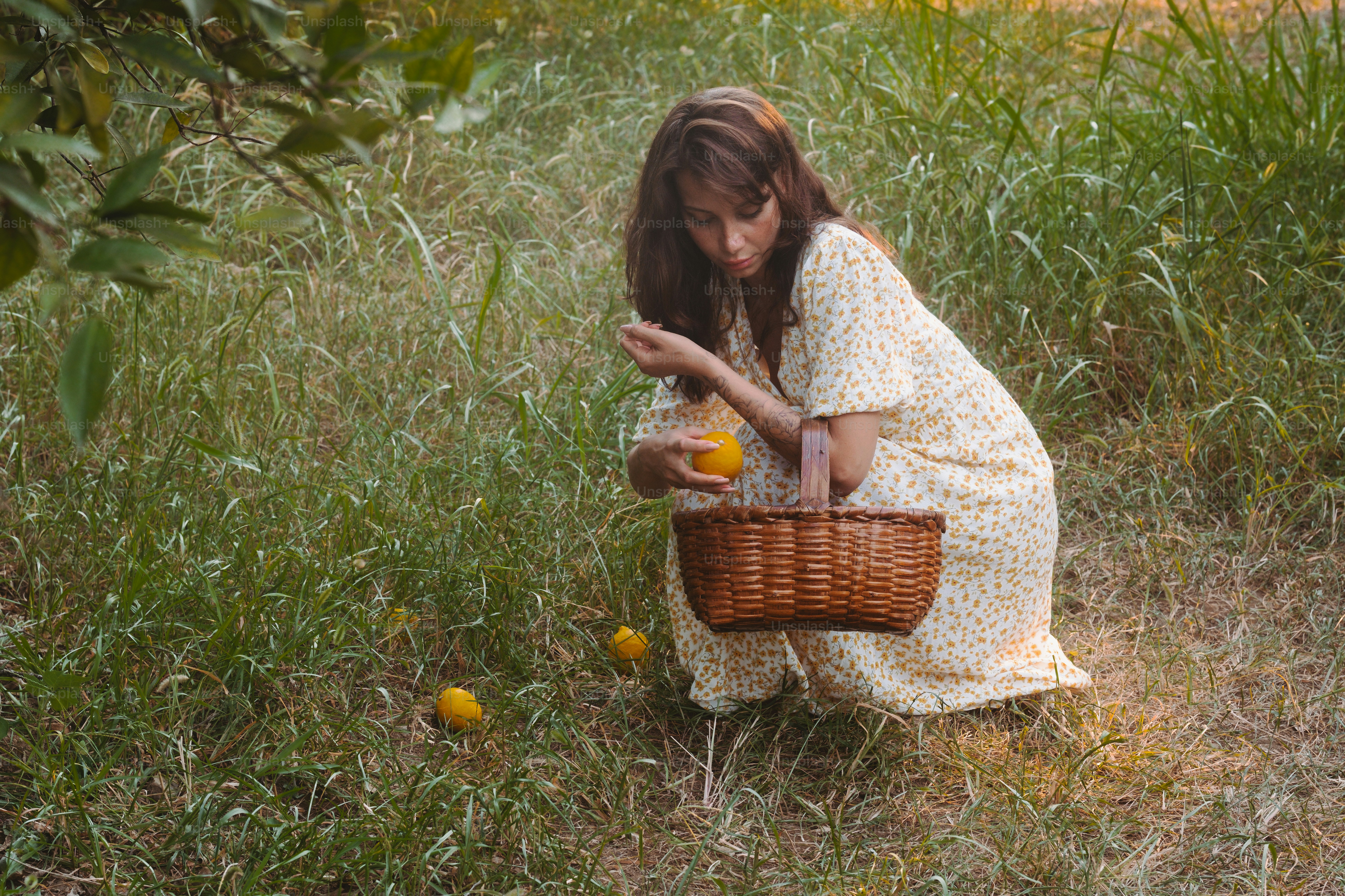 A woman kneeling down in a field with a basket of fruit