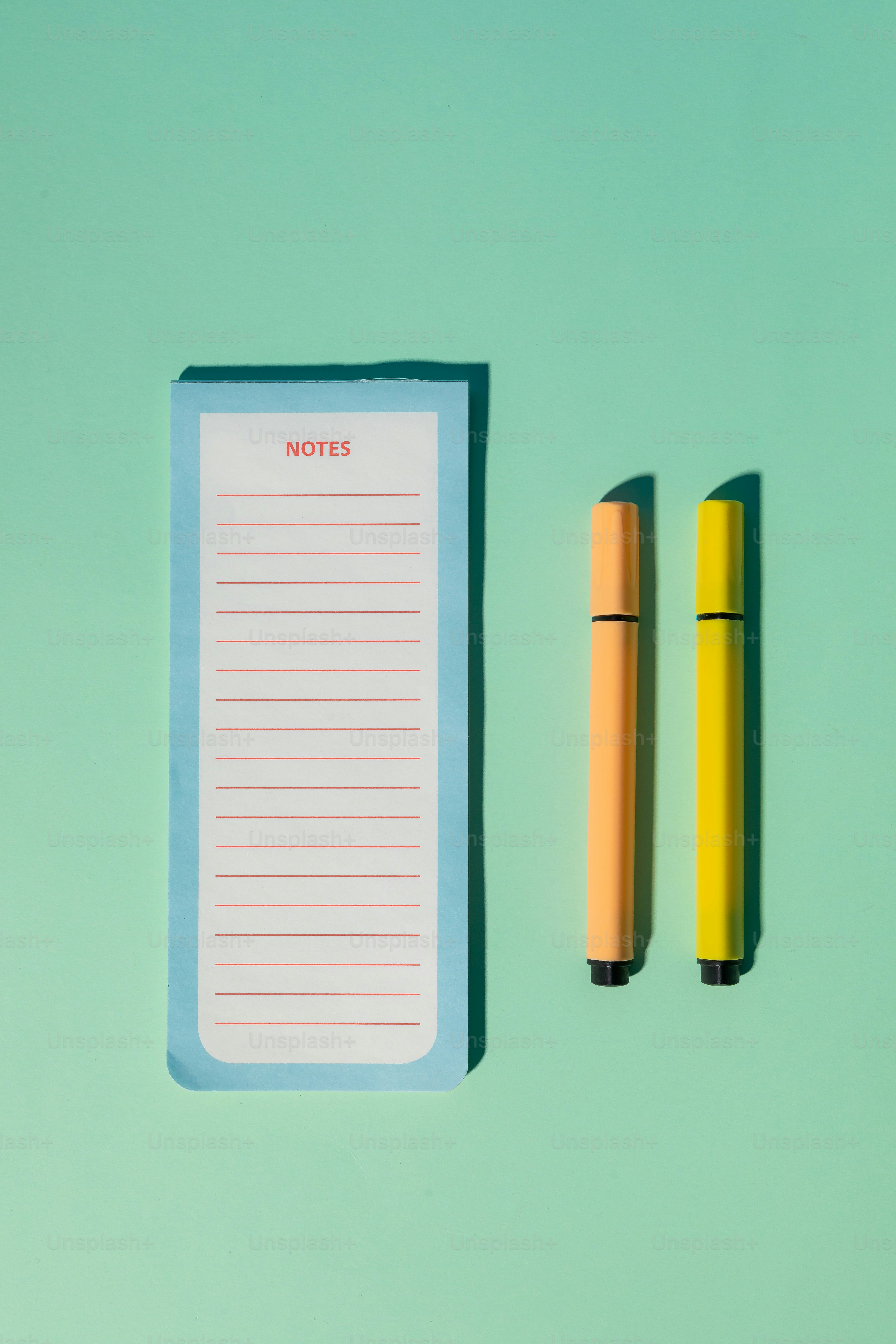 A notepad, pen and a pair of scissors on a green background