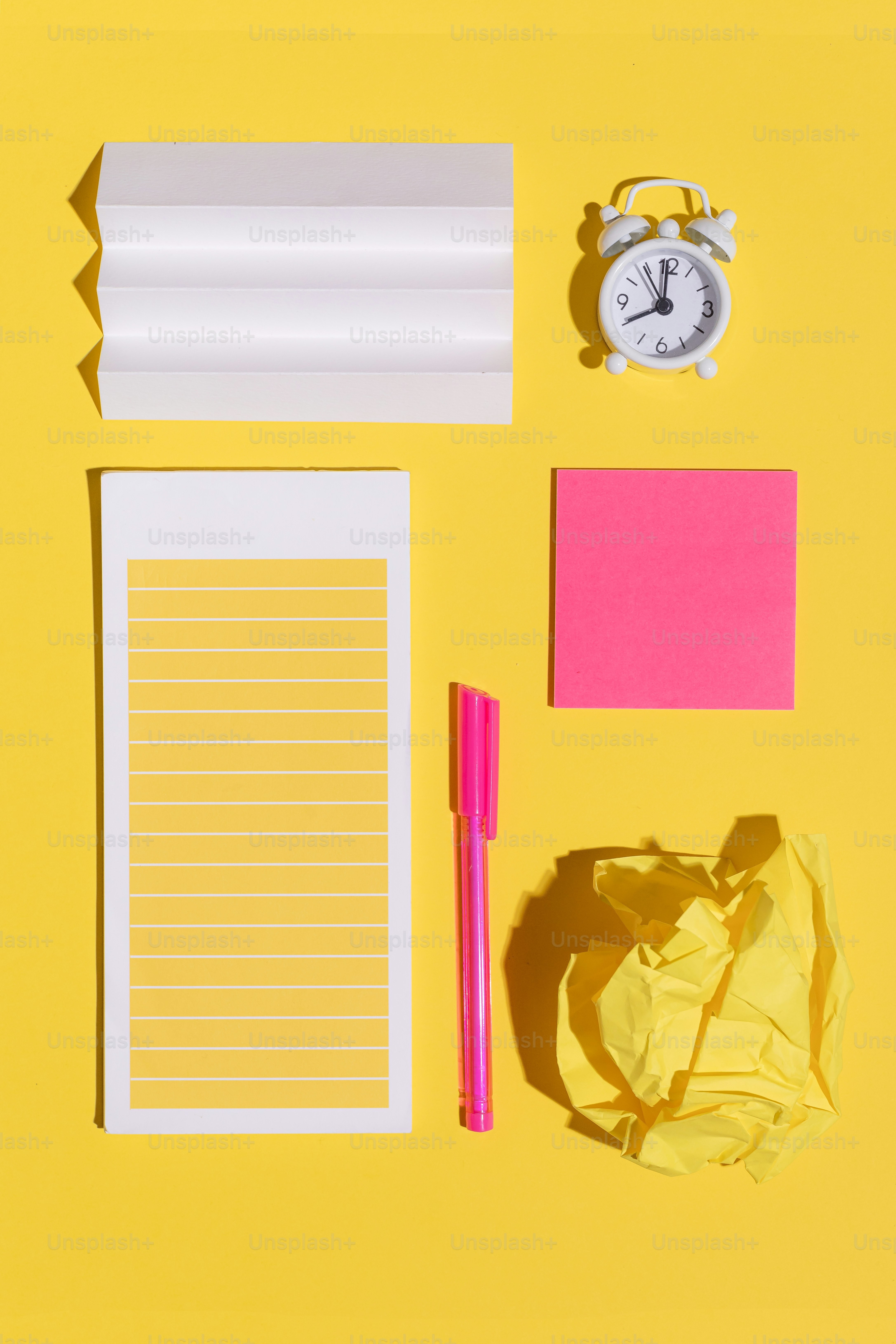A yellow desk with a clock, notepad, pen and paper