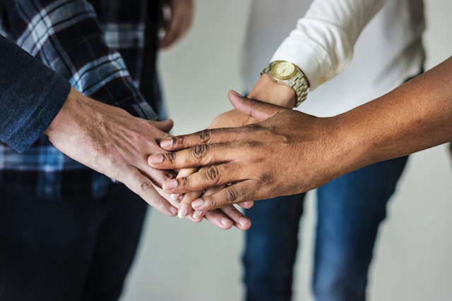 A circle of diverse hands joined in the middle of a group huddle.