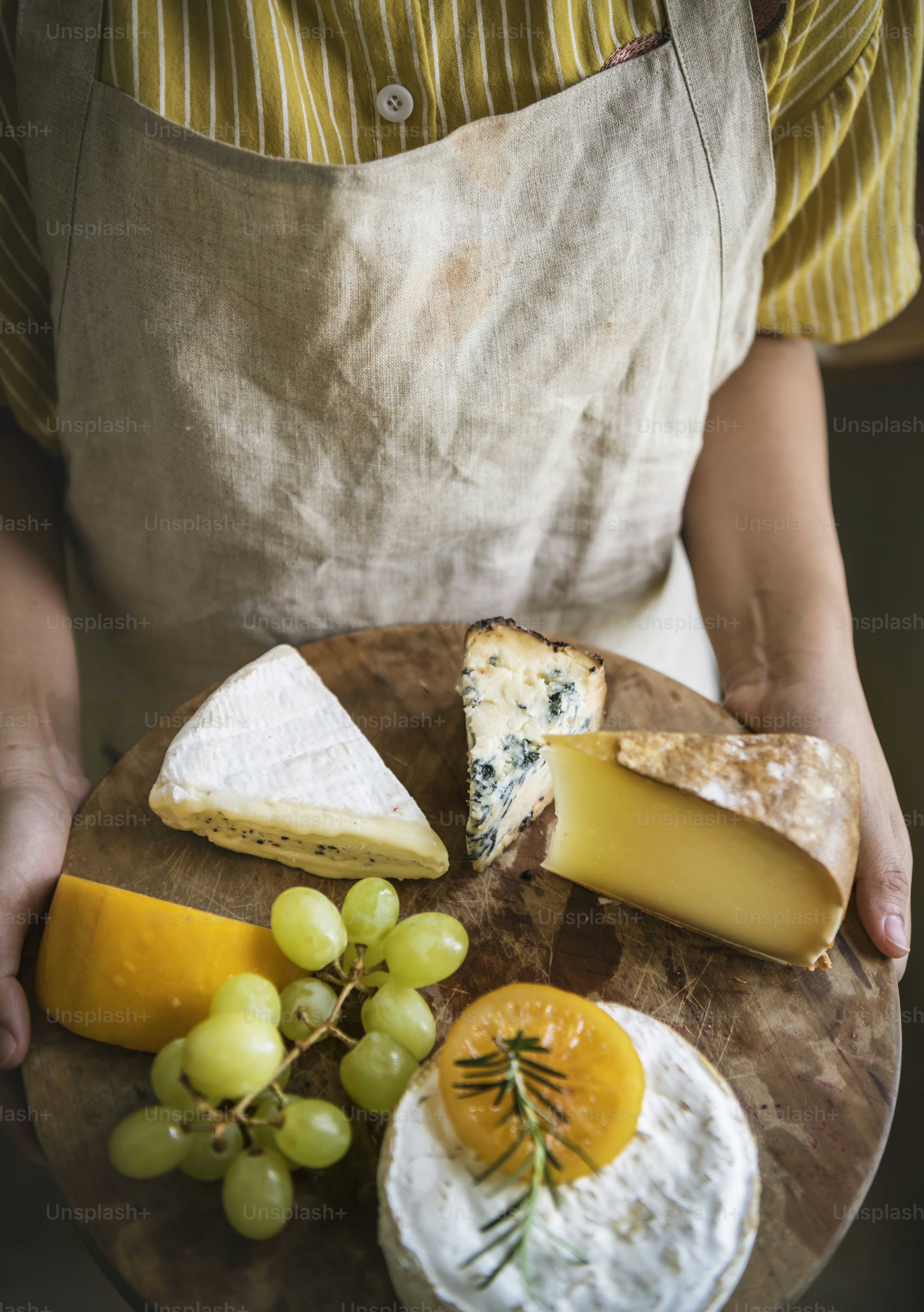 Personne tenant un plateau de raisins verts et différents types de fromage