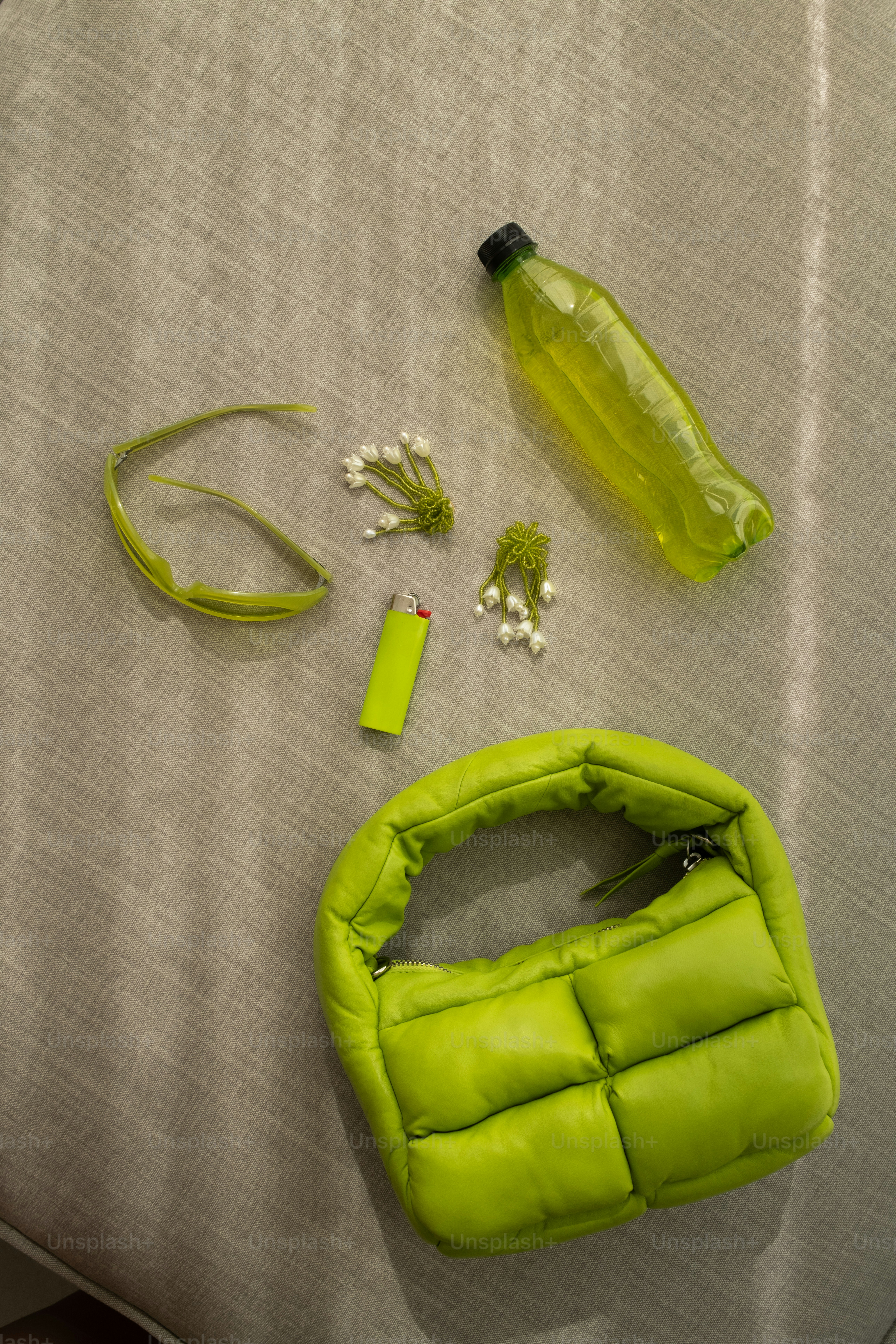 A green purse sitting on top of a bed next to a bottle