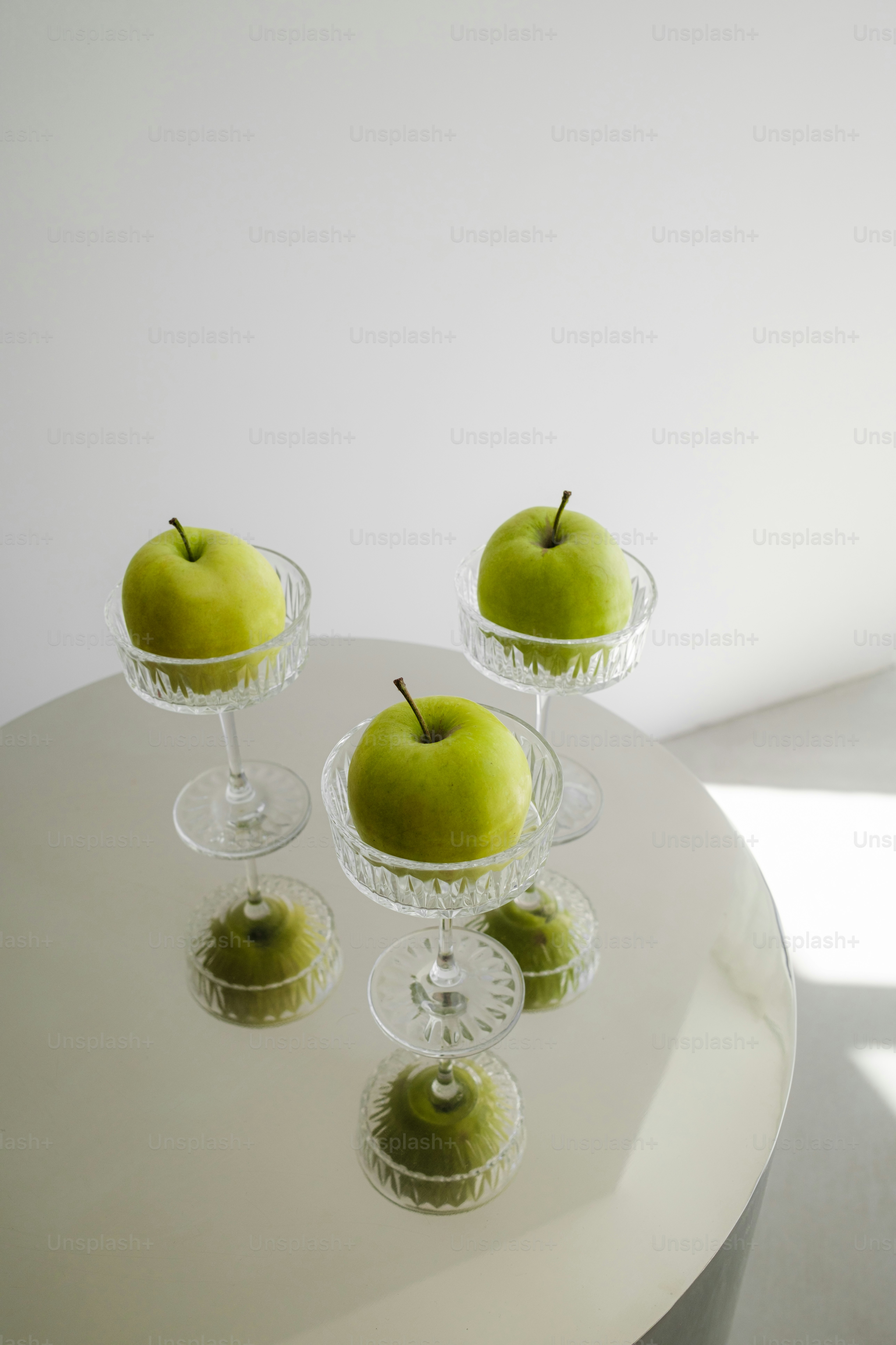 A white table topped with three glasses filled with green apples