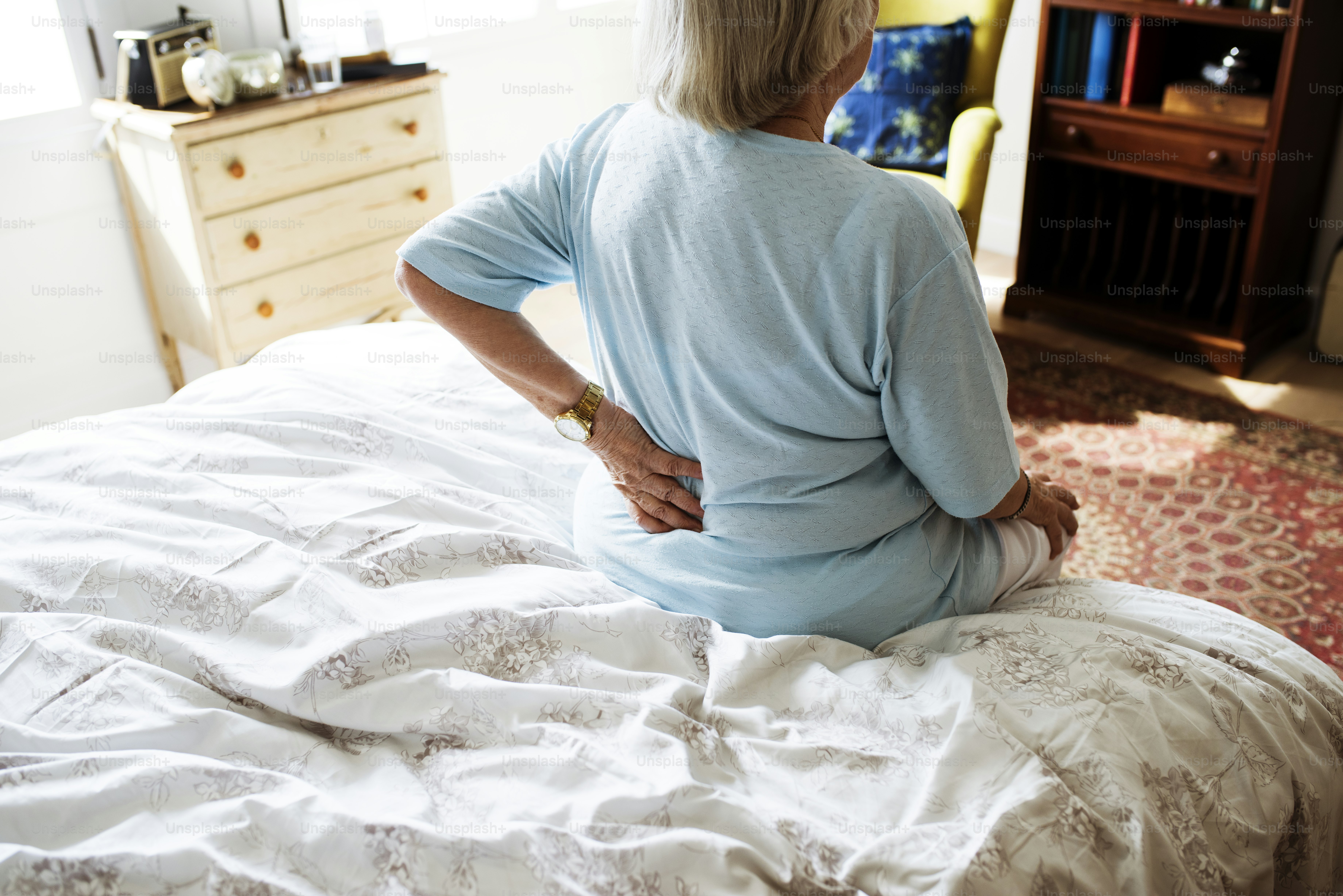 Femme âgée assise sur le lit en douleur
