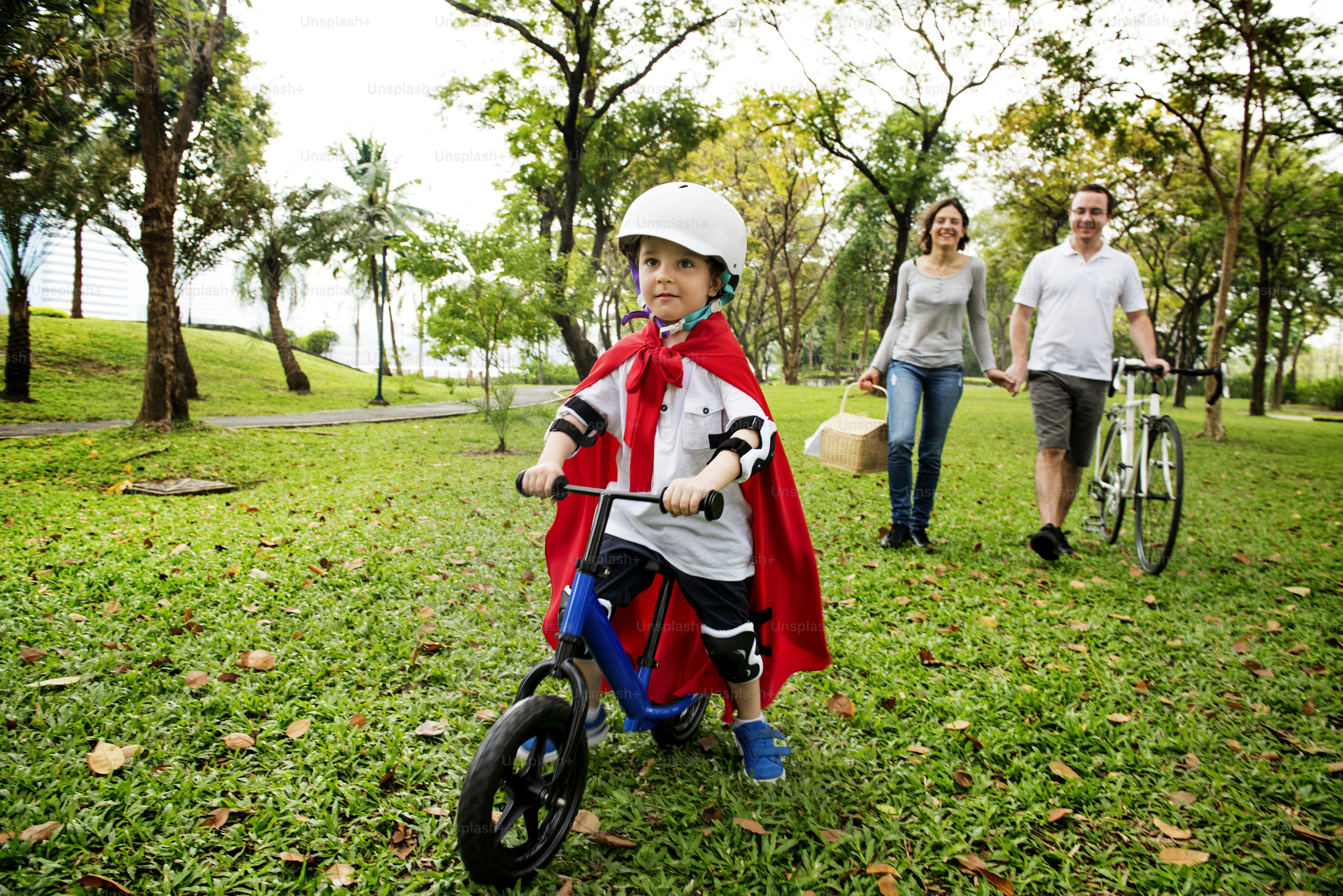 公園で家族と自転車に乗るスーパーヒーローの小さな男の子
