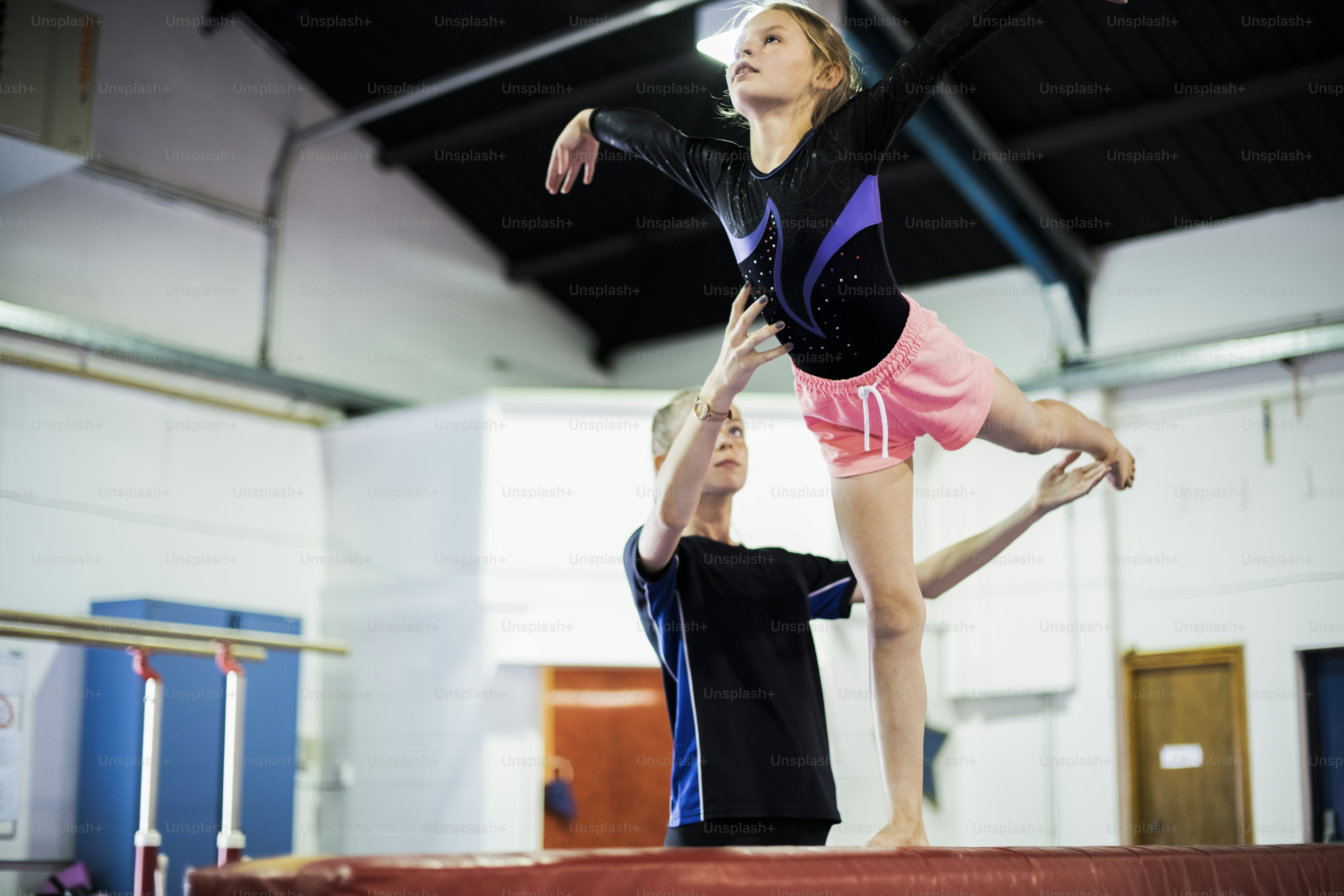 Coach training young gymnast to balance on a balance beam