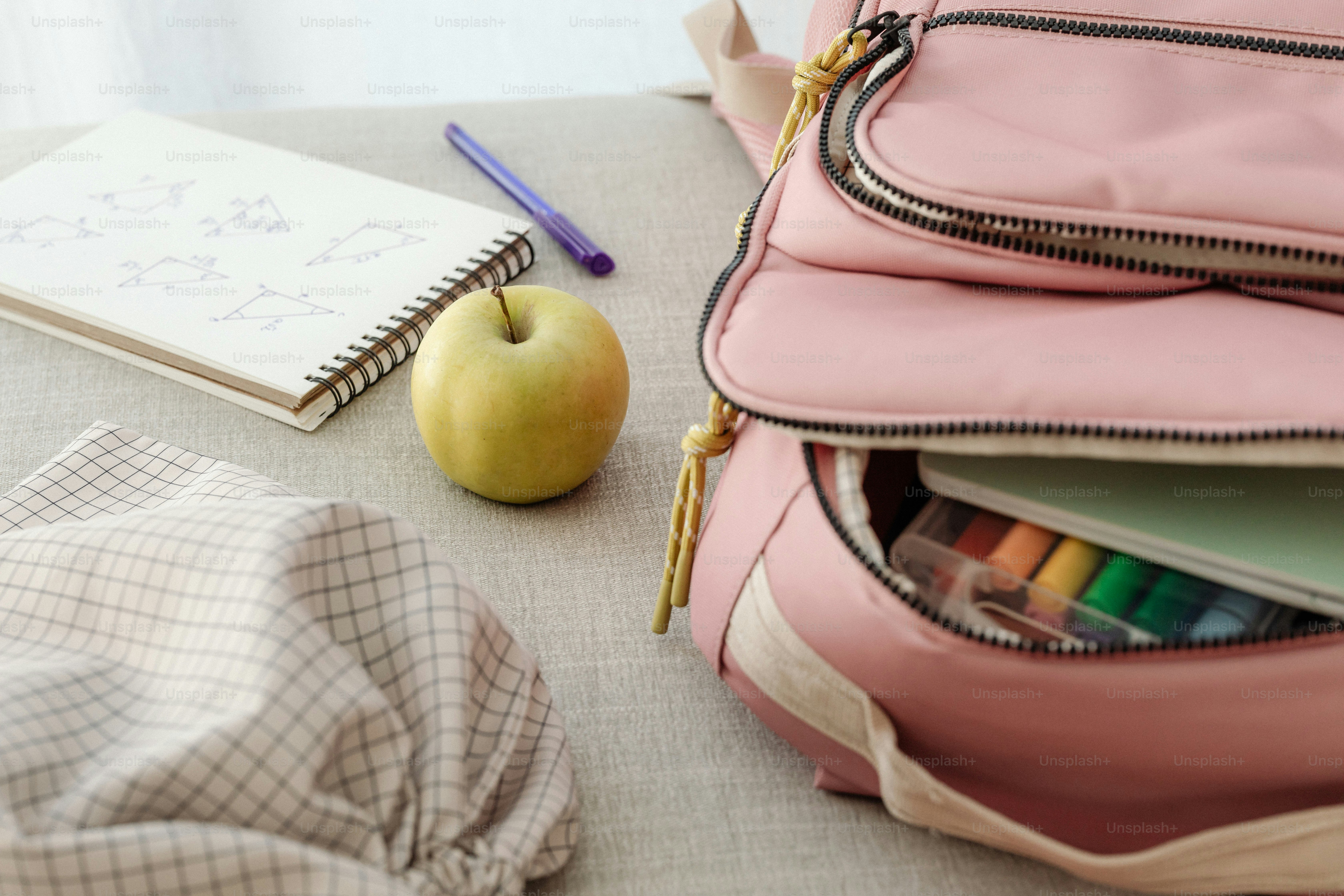 A pink backpack sitting on top of a table next to an apple