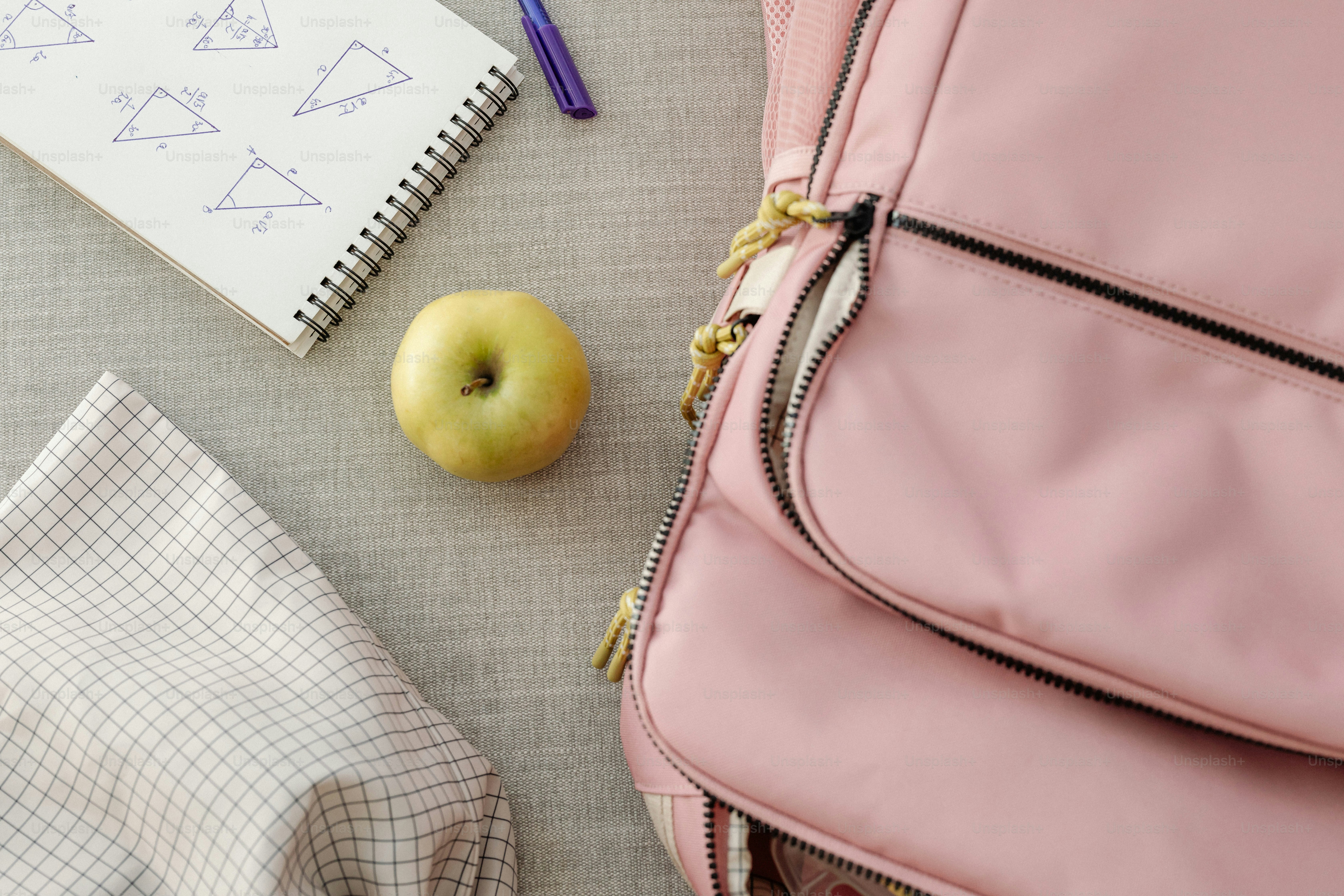 A pink backpack sitting on top of a table next to an apple