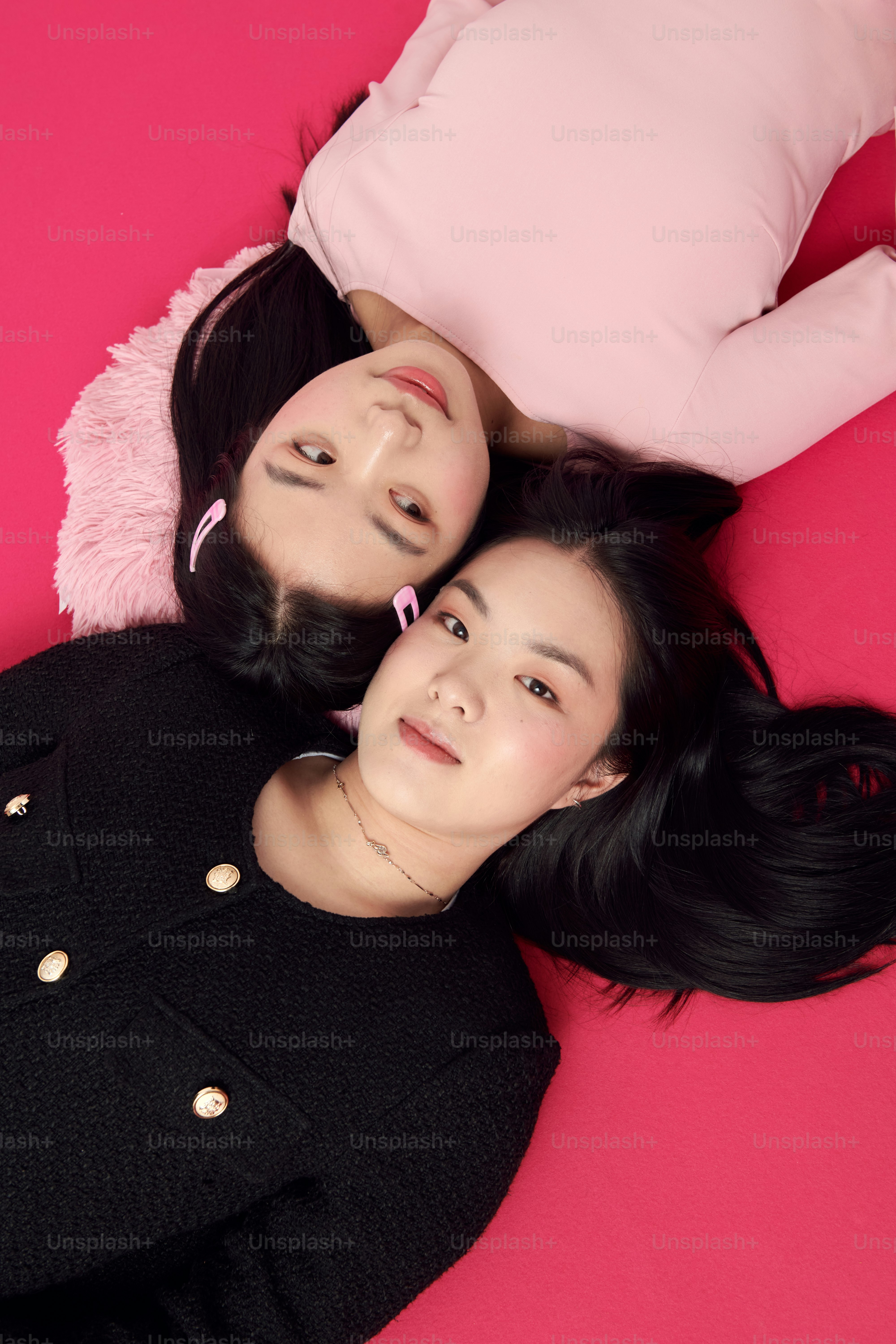 Two asian women laying on a pink surface