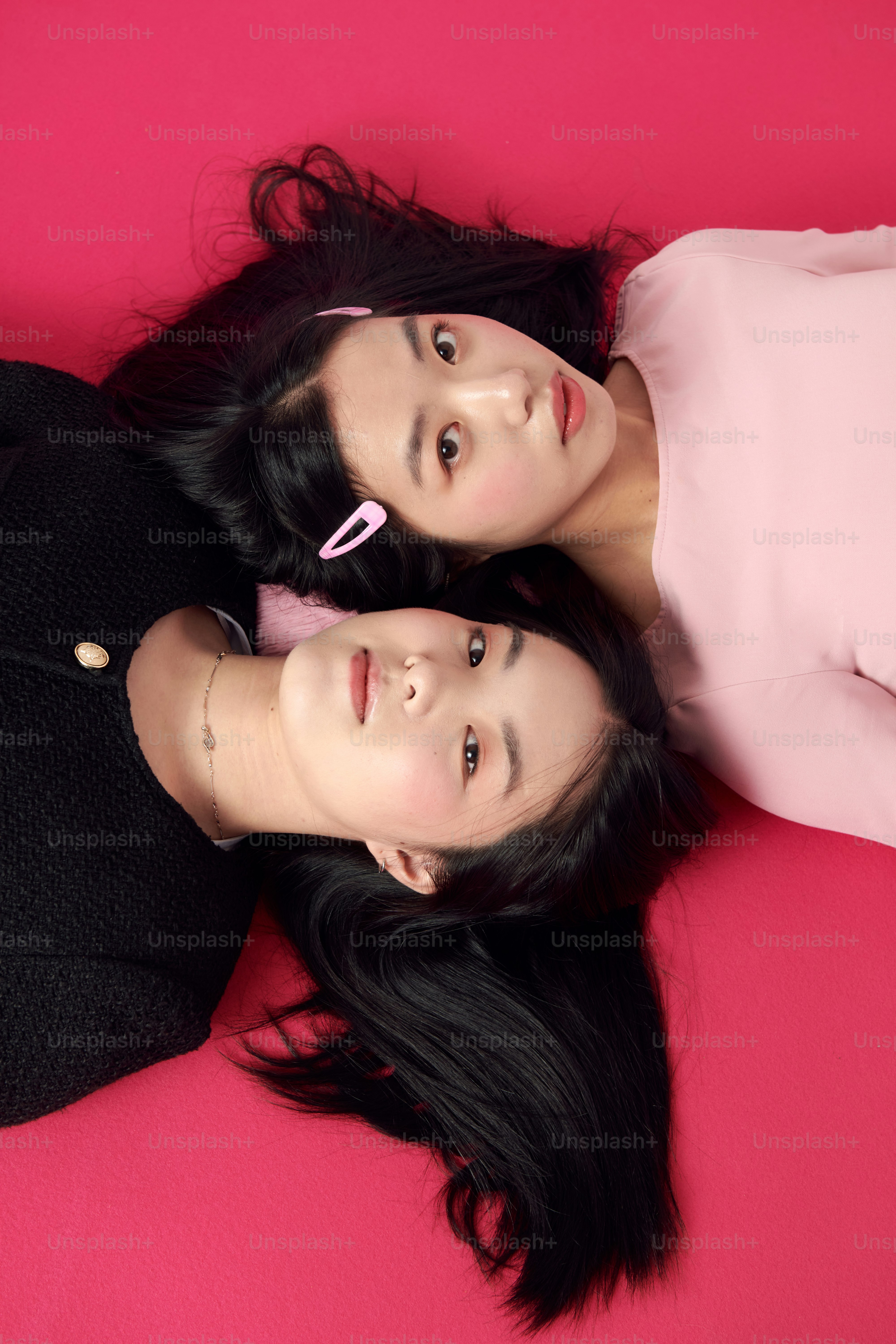 Two young women laying on a pink surface