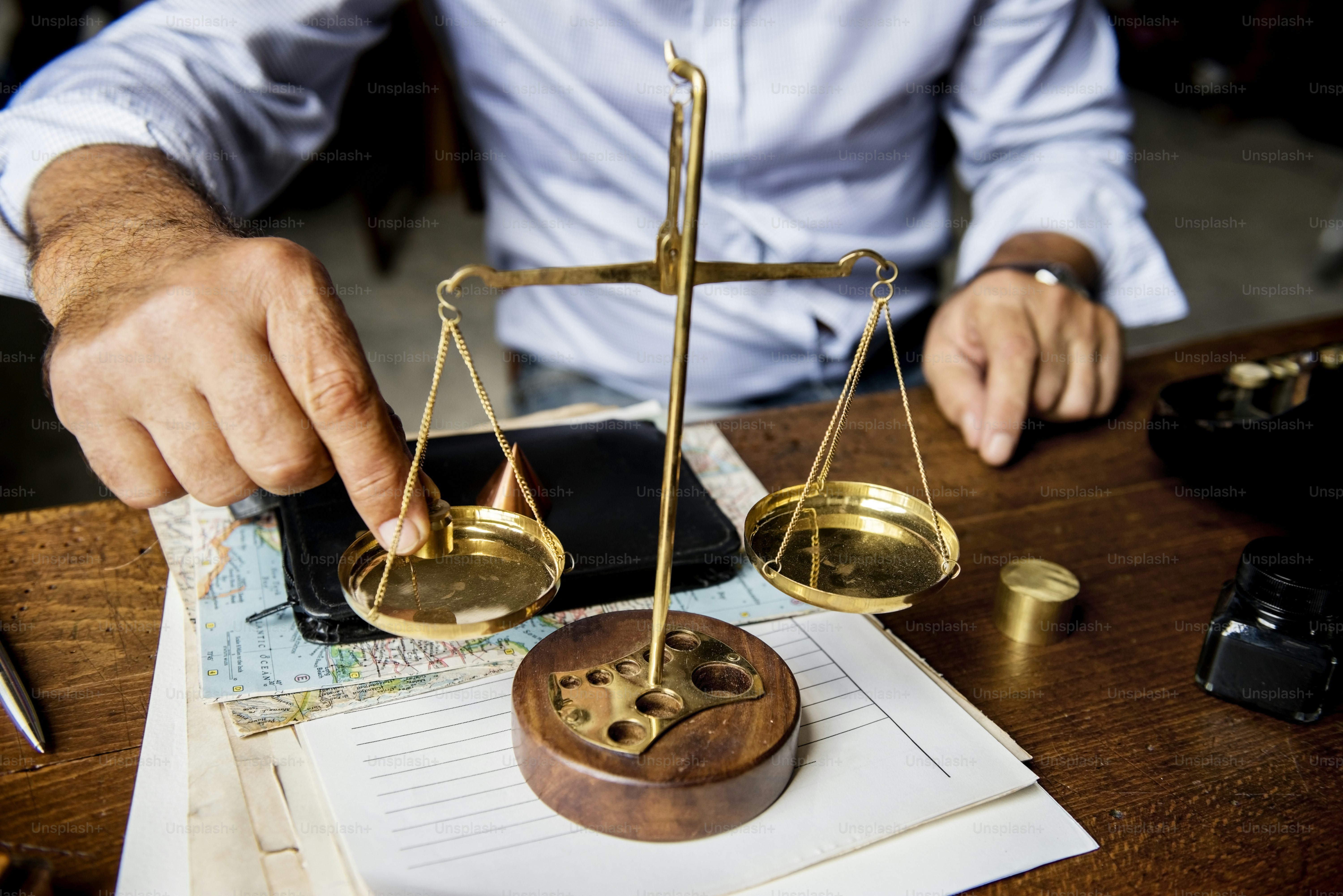 A person adjusting a brass balance scale on a wooden desk with papers