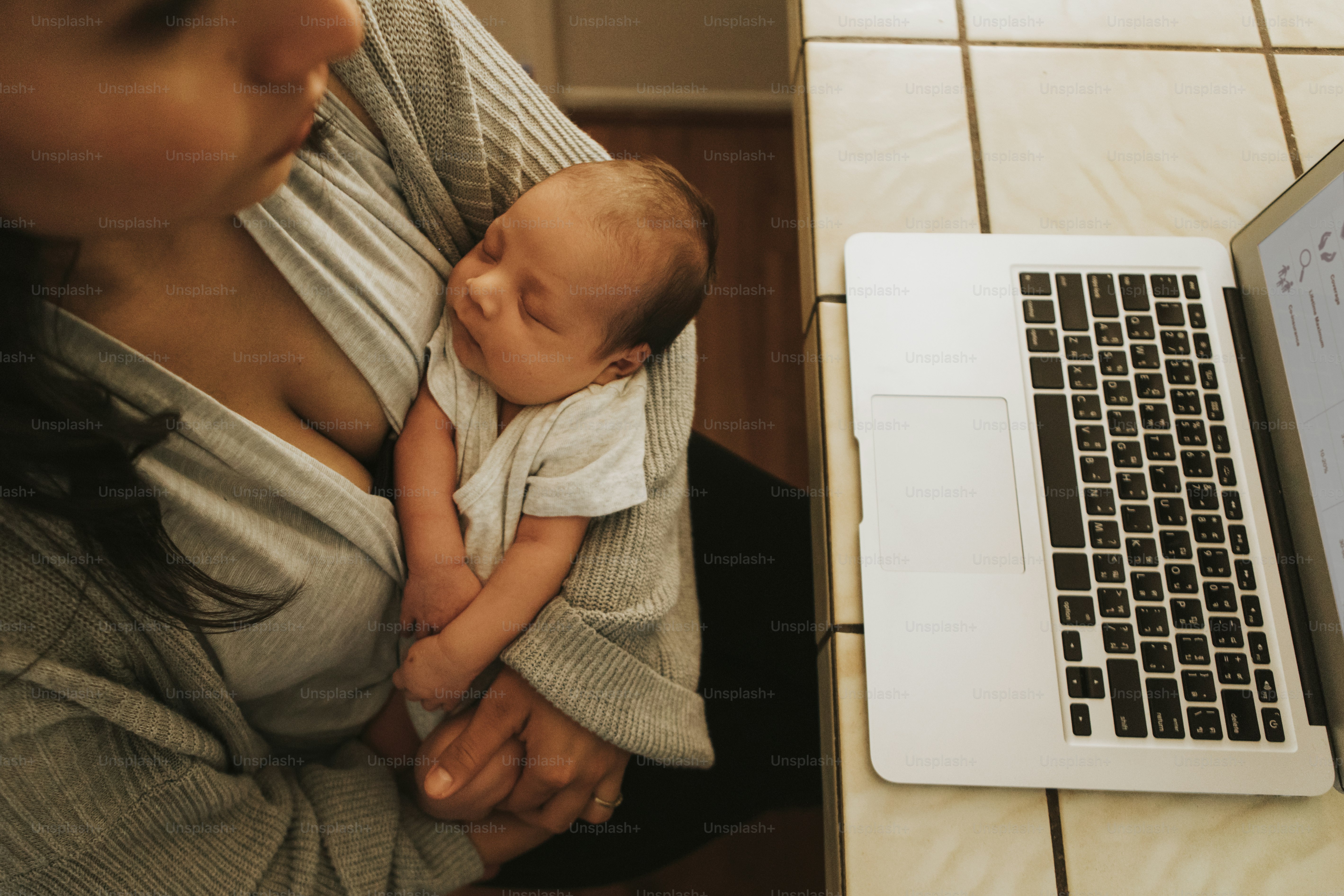 Mutter an einem Computer und mit ihrem Baby im Arm