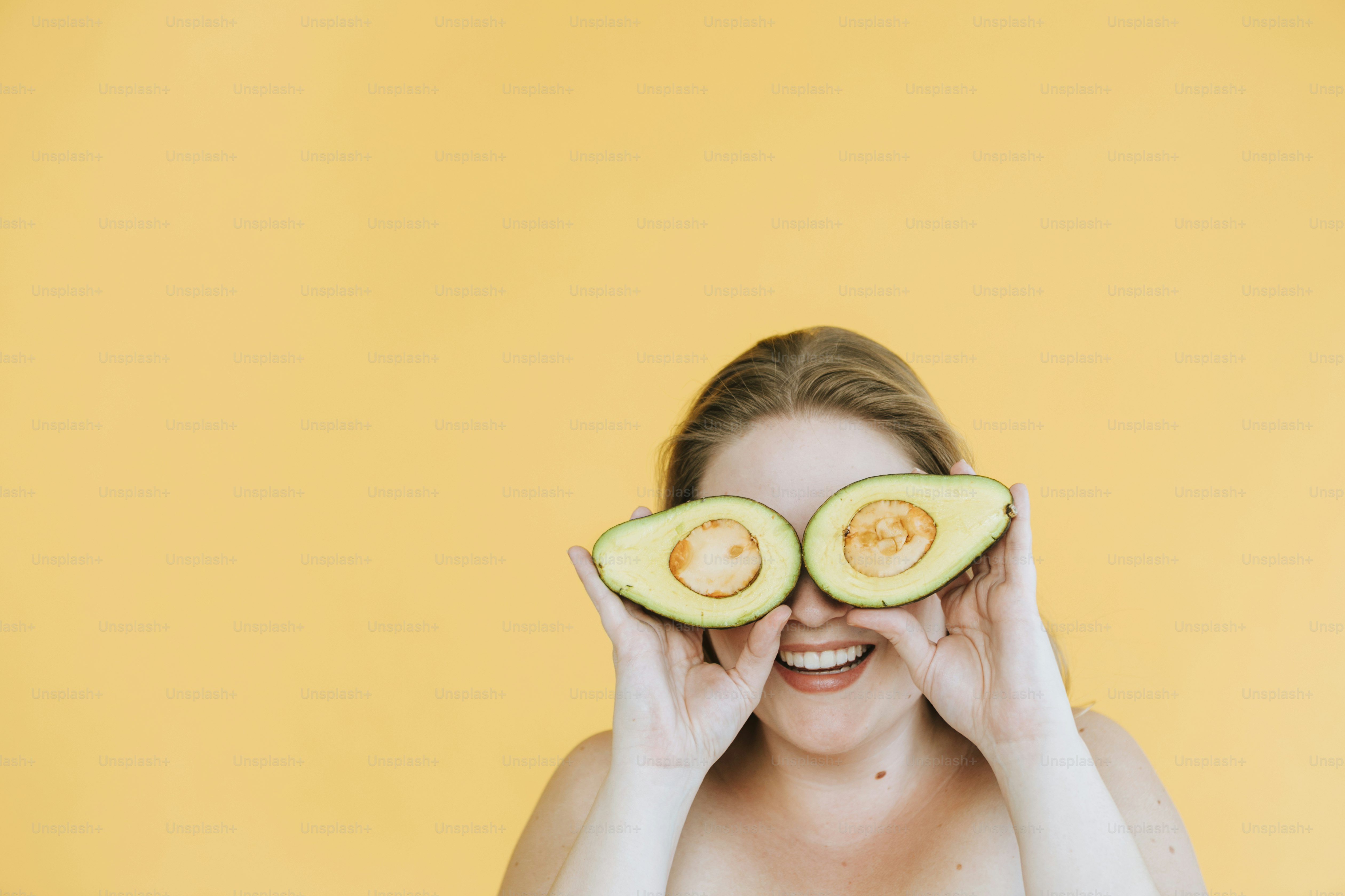 Happy woman holding freshly cut avocados over her eyes