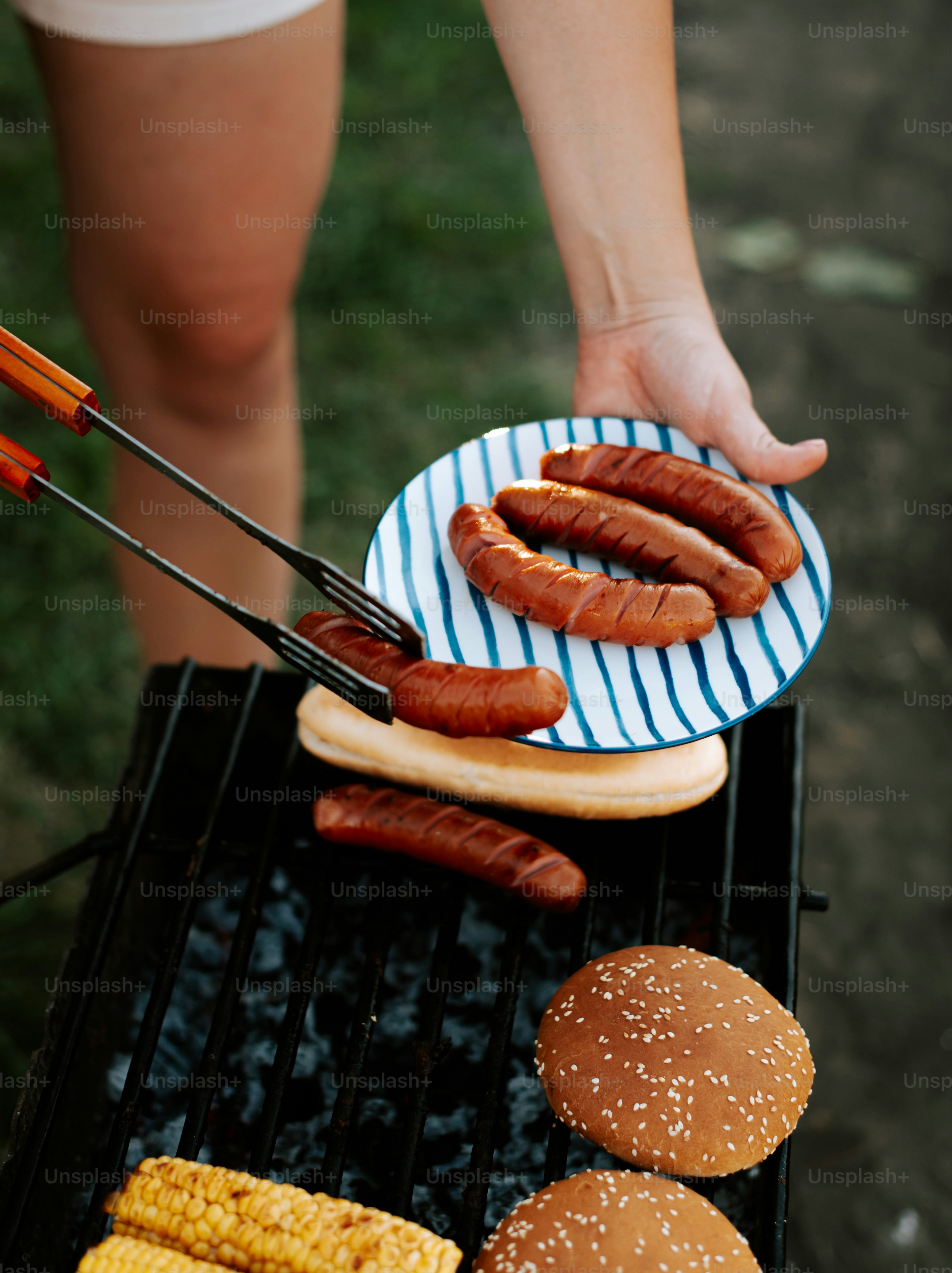 A person cooking hot dogs and hamburgers on a grill
