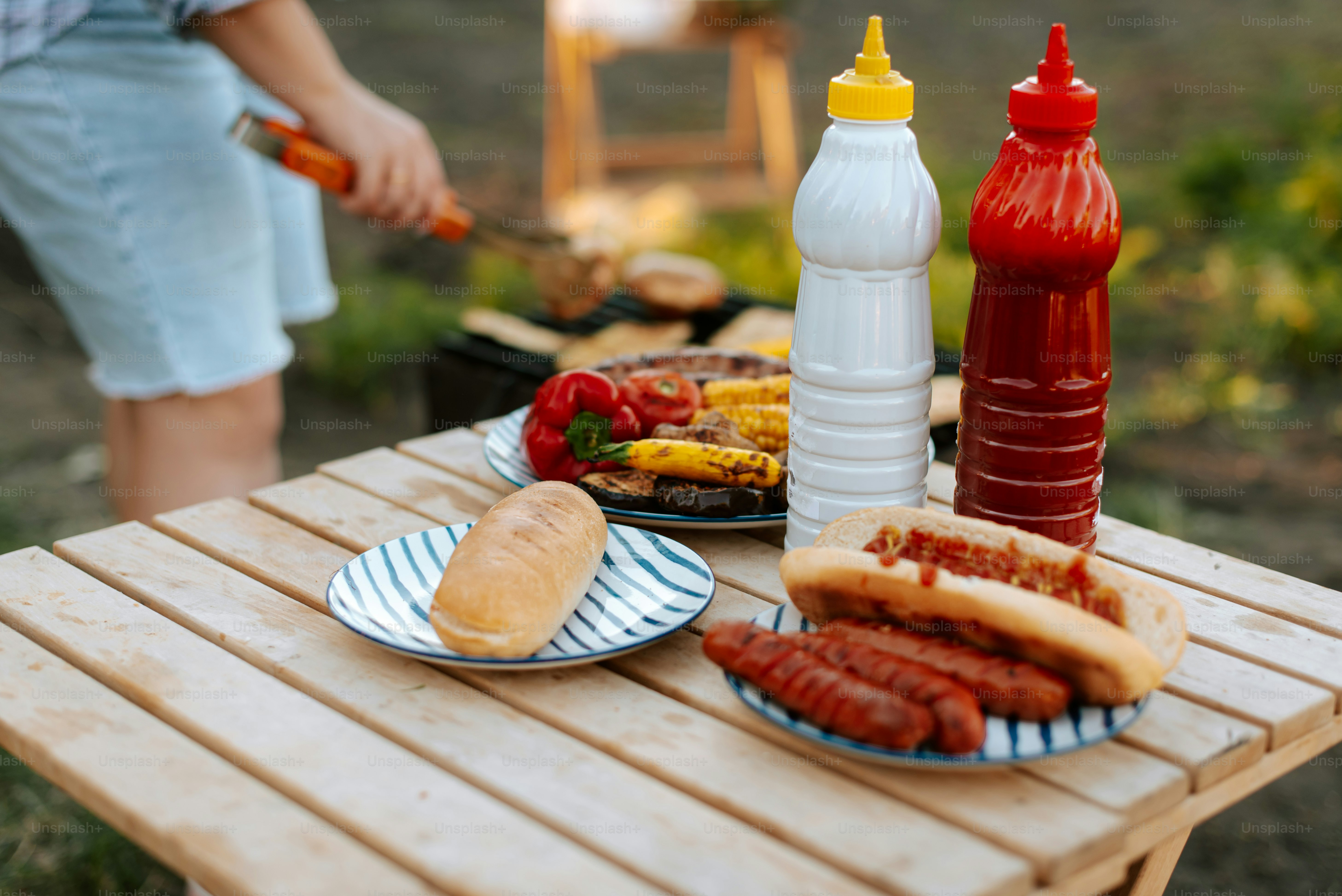A picnic table with hot dogs, ketchup, mustard and ketchup