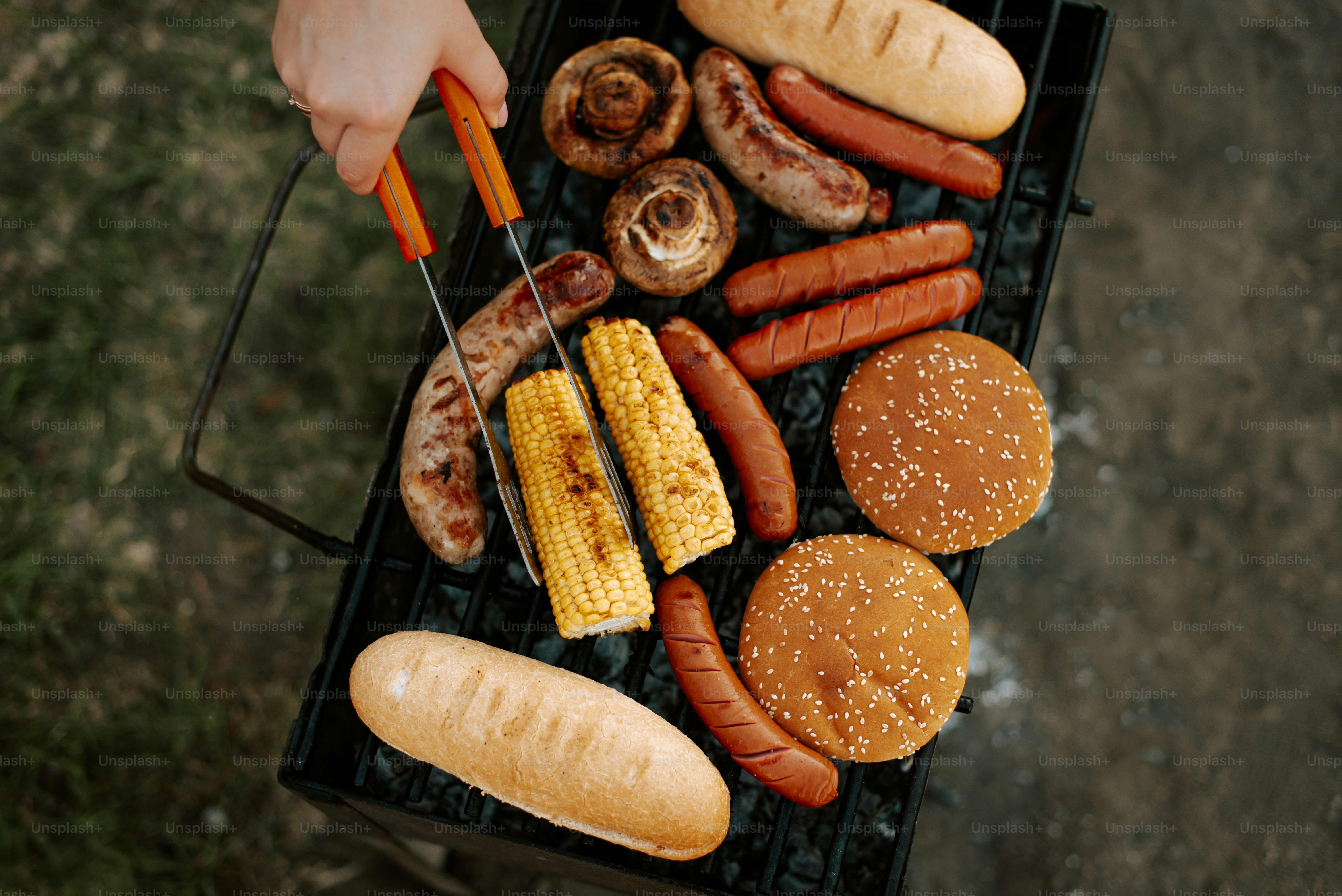 A grill with hot dogs, hamburgers and corn on the cob