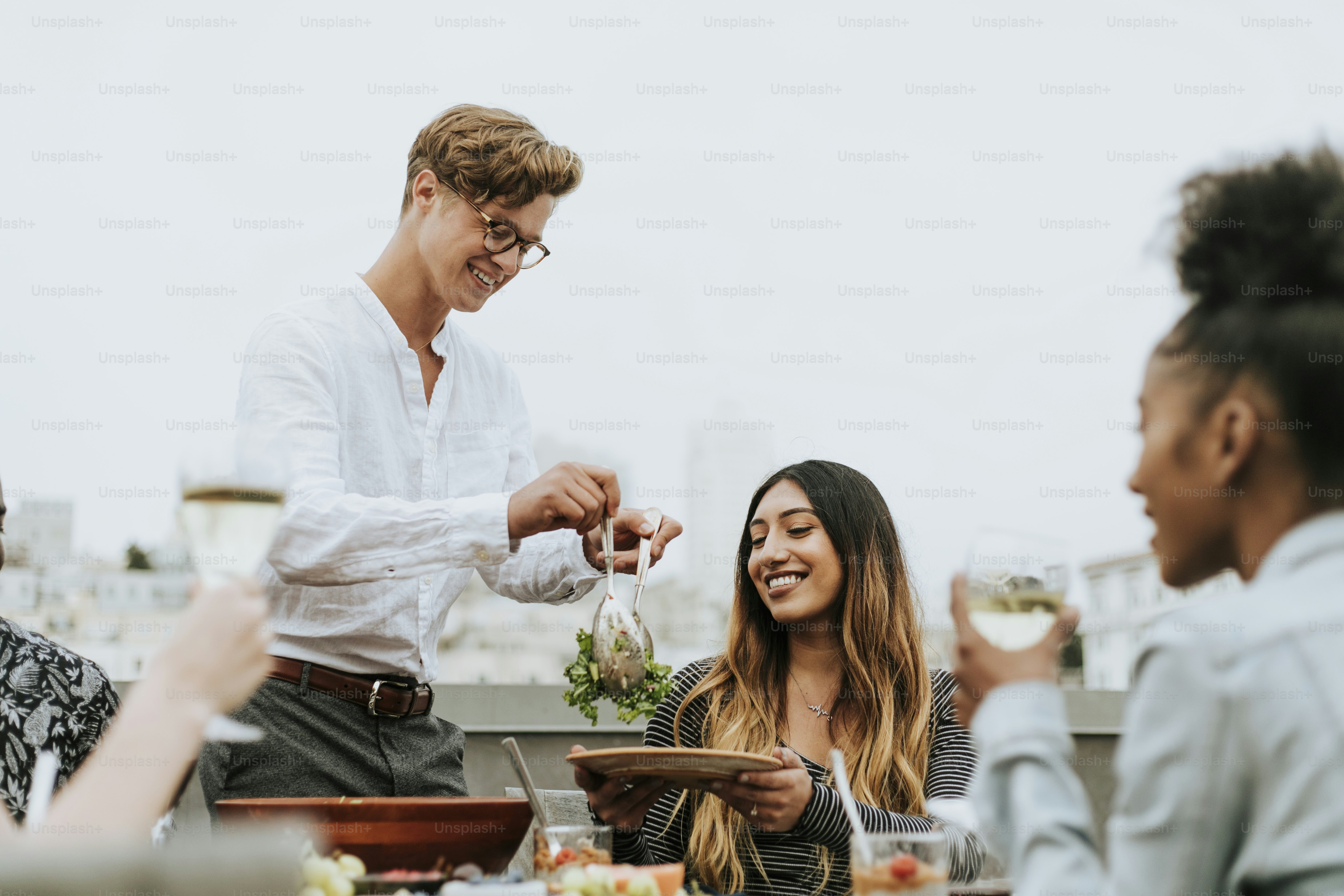 Man serving his friends salad at a rooftop party