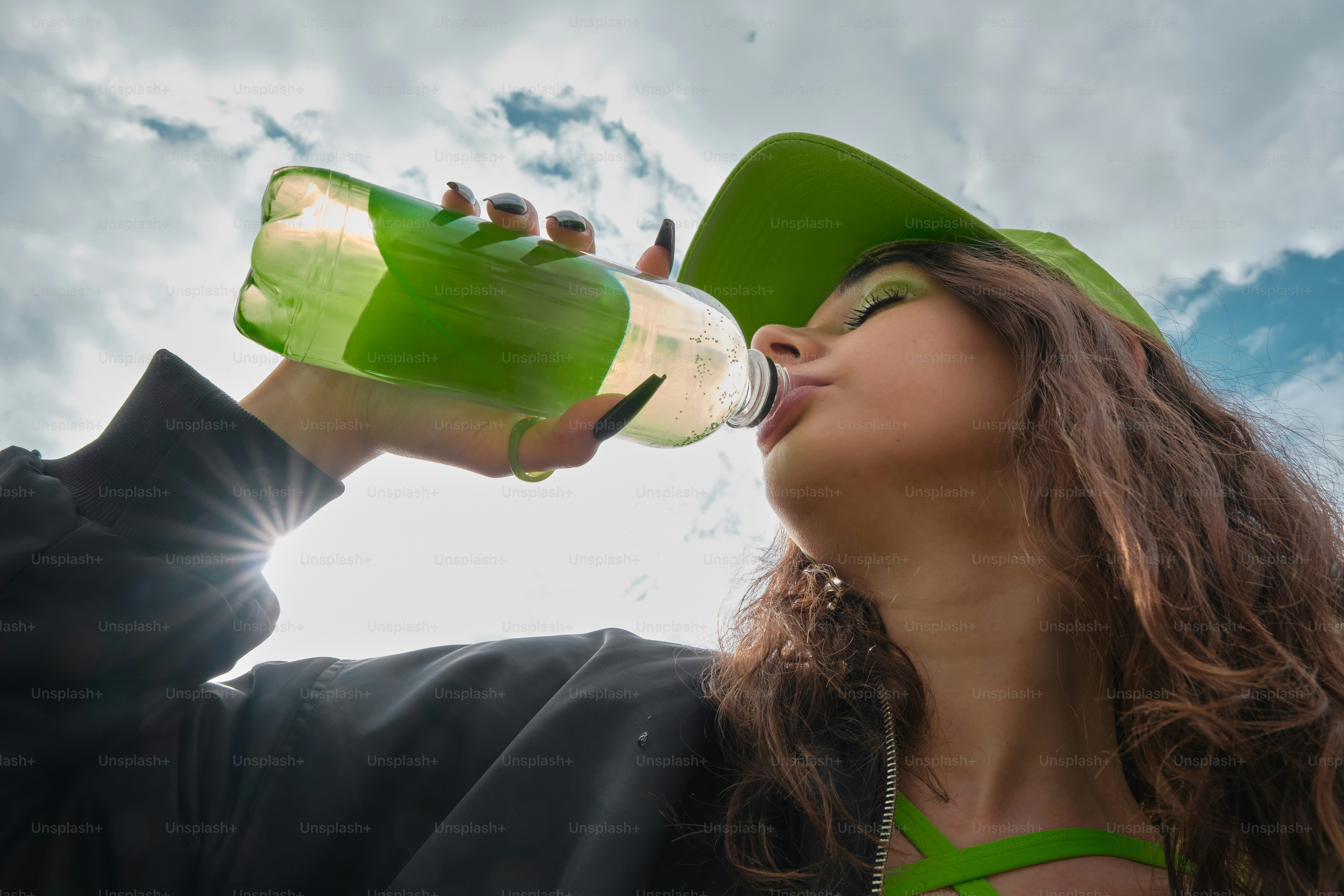 A woman wearing a green hat drinking from a bottle